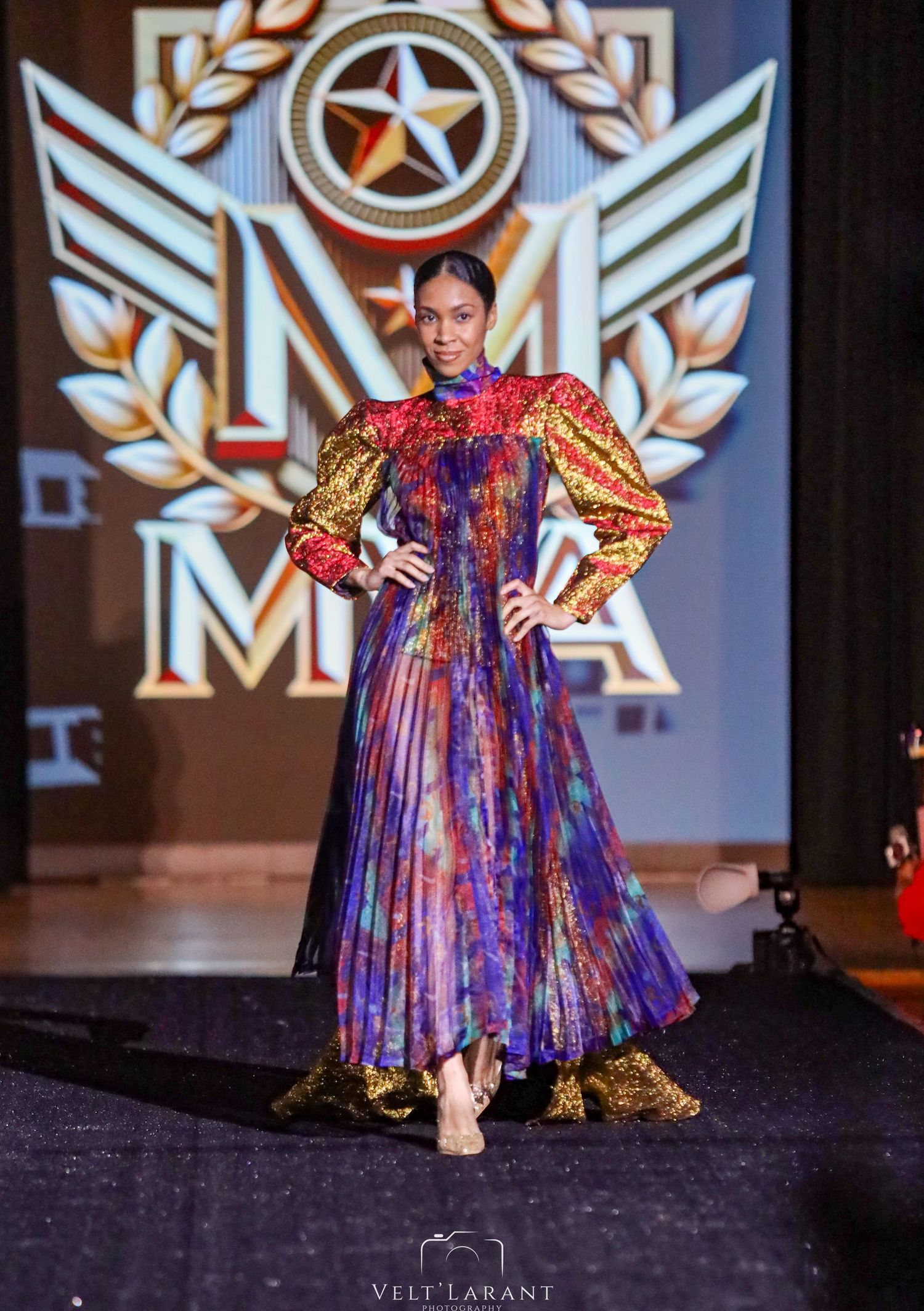Model showcases dramatic purple and gold dress with puffy sleeves on fashion runway.