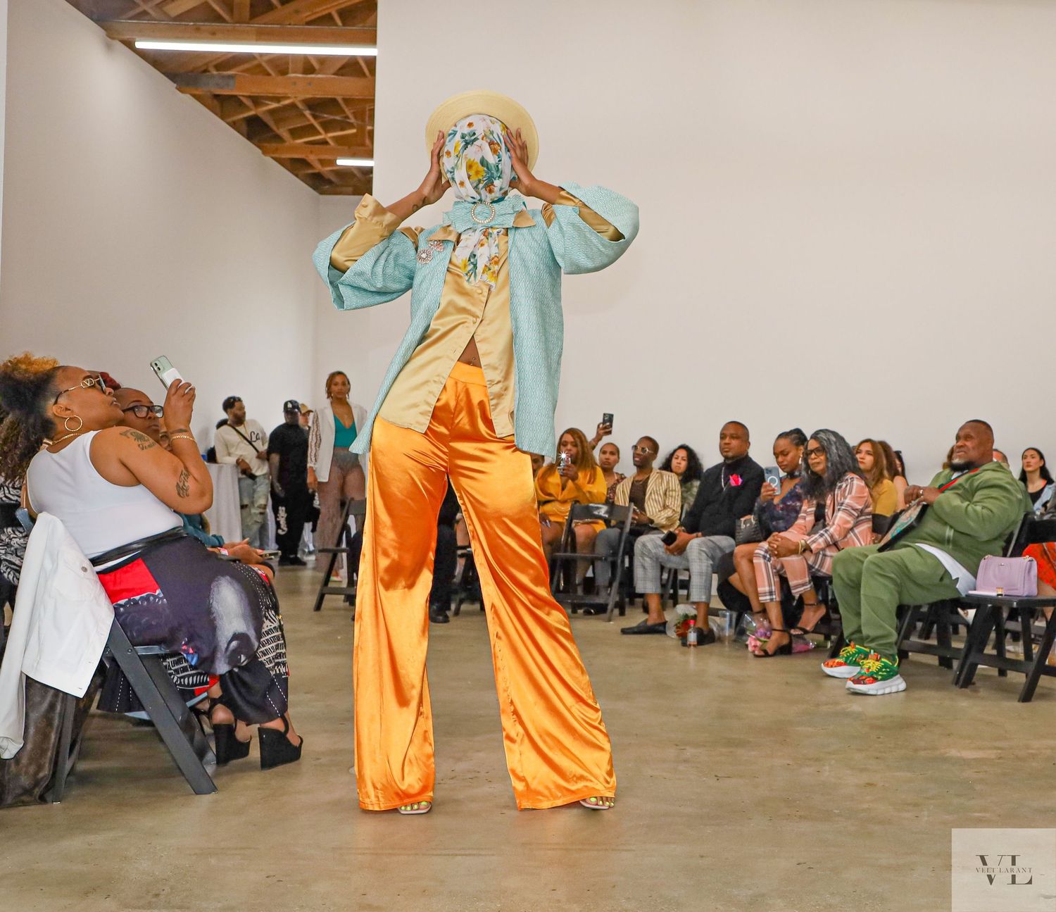 Performance or dance scene with flowing orange costumes in a gallery-like space with seated audience.