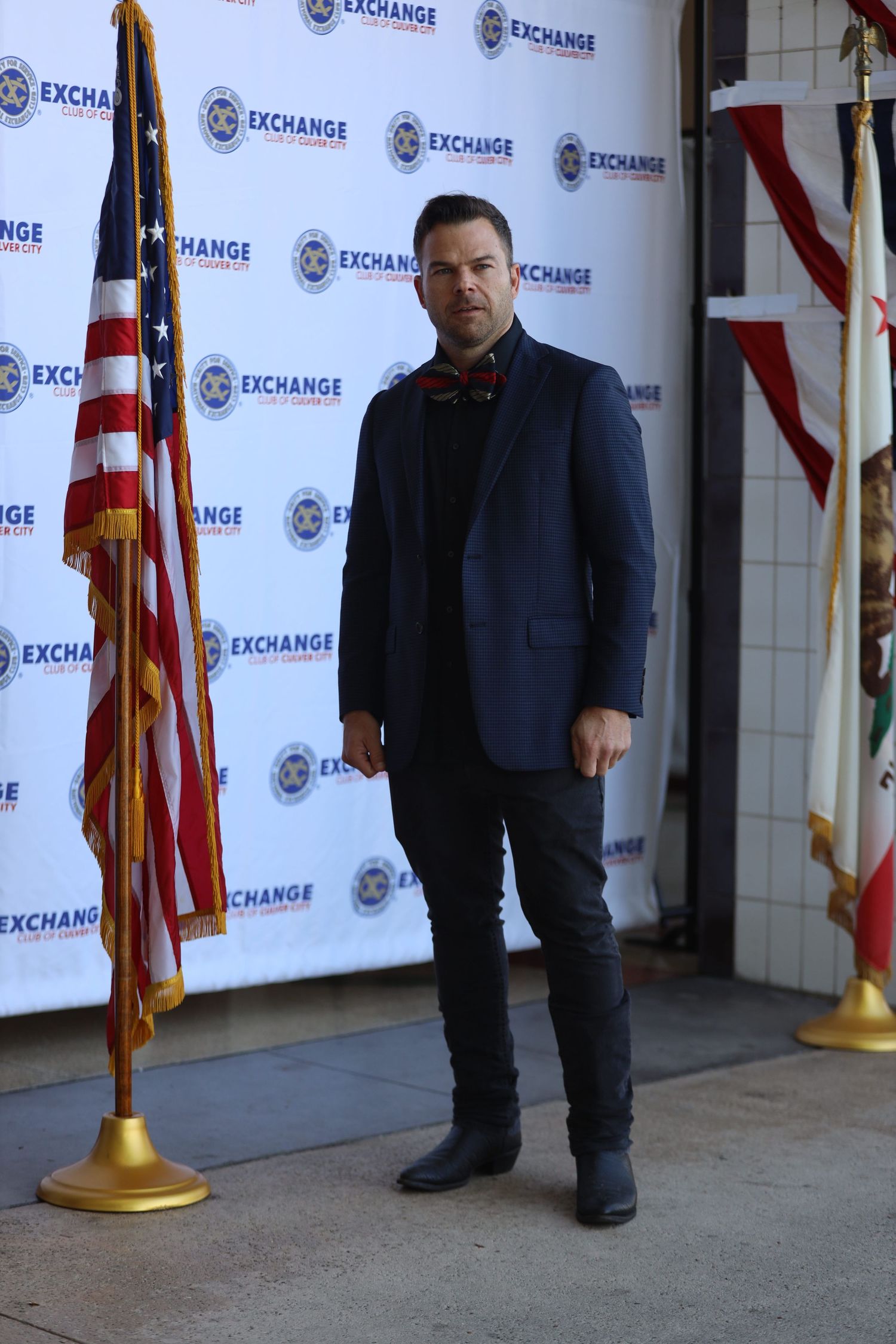 Person in dark attire poses at promotional event with American flags.