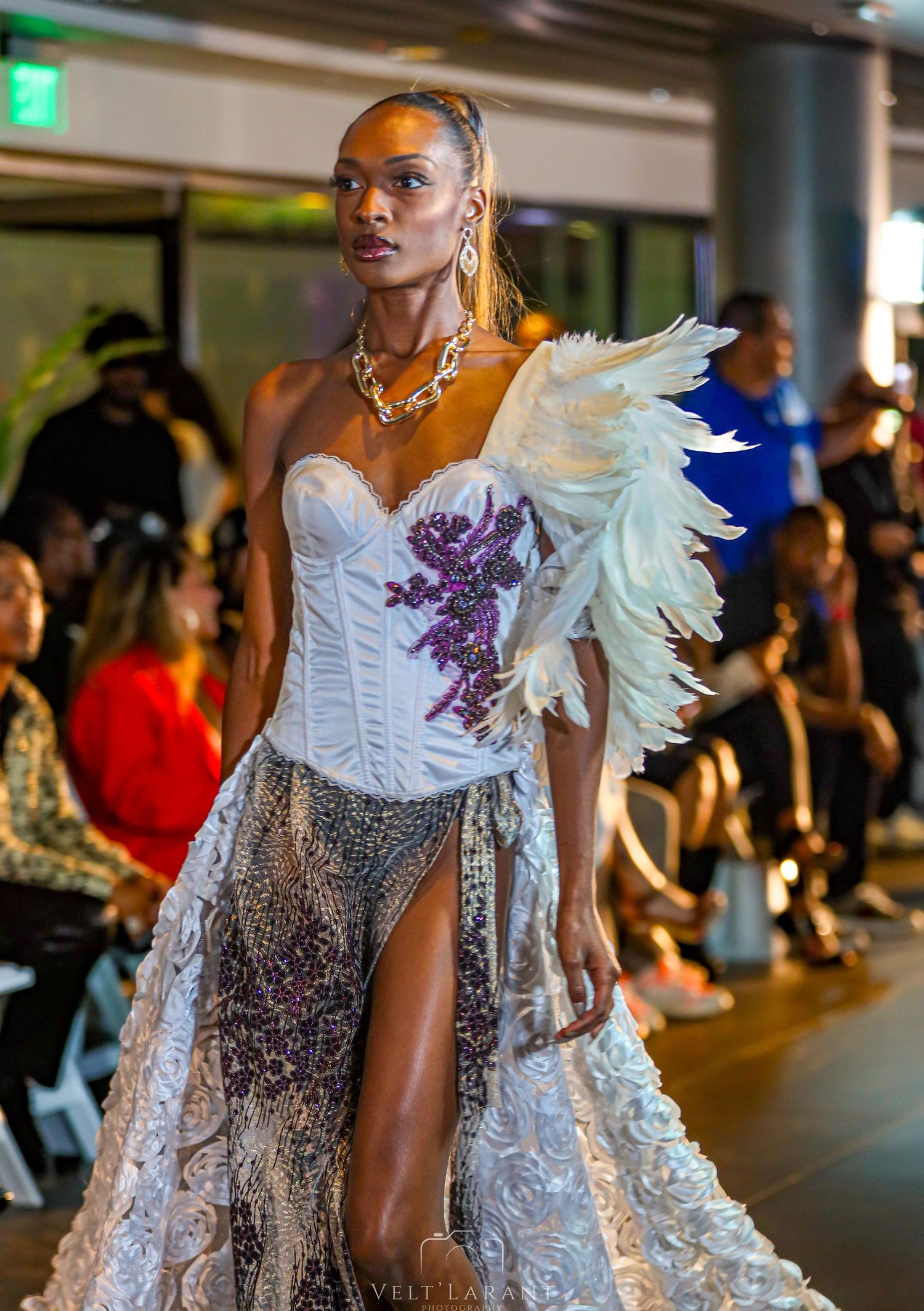 Model walks runway in avant-garde white dress with feather details and purple accents.