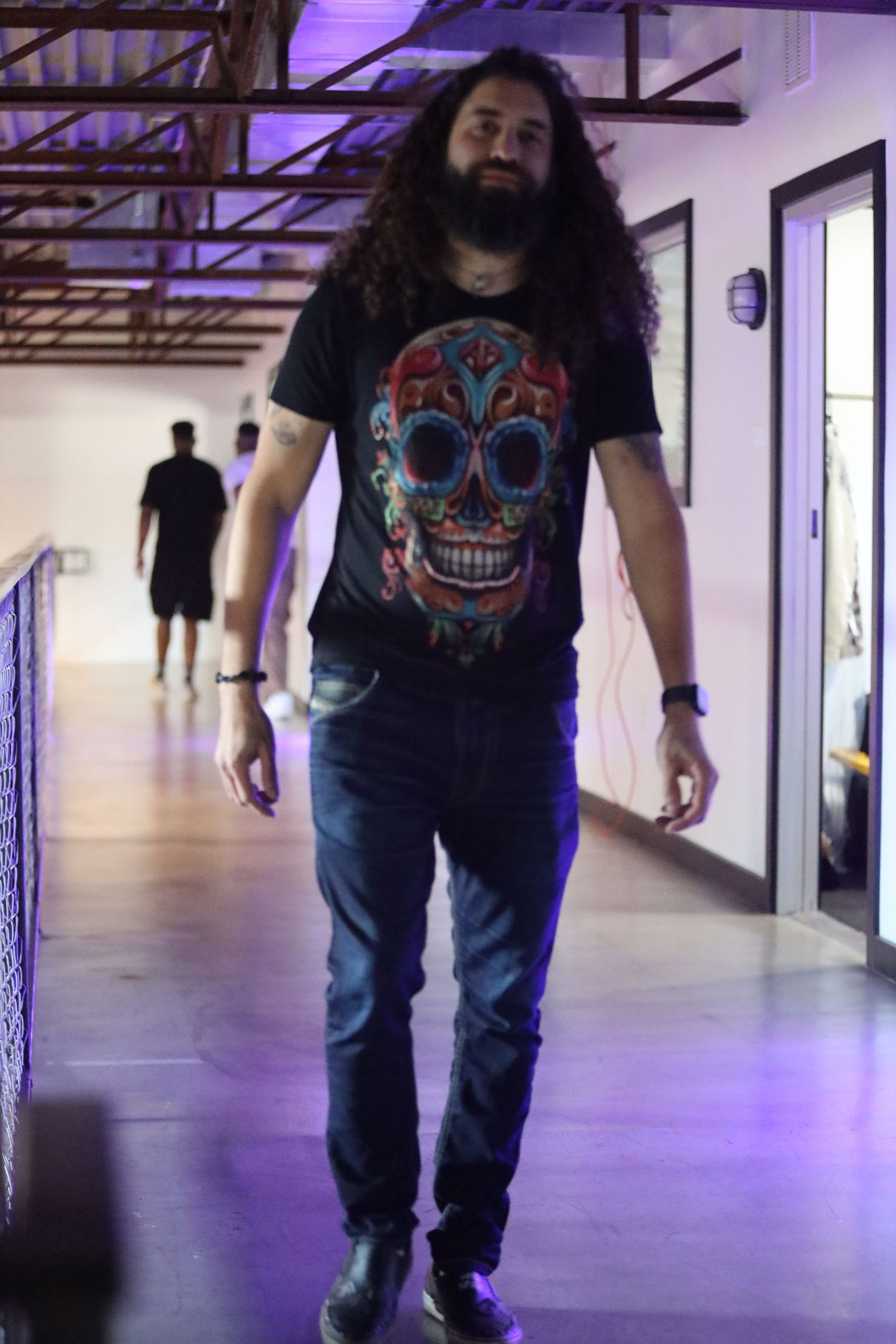 Person wearing sugar skull graphic t-shirt and jeans in purple-lit hallway.