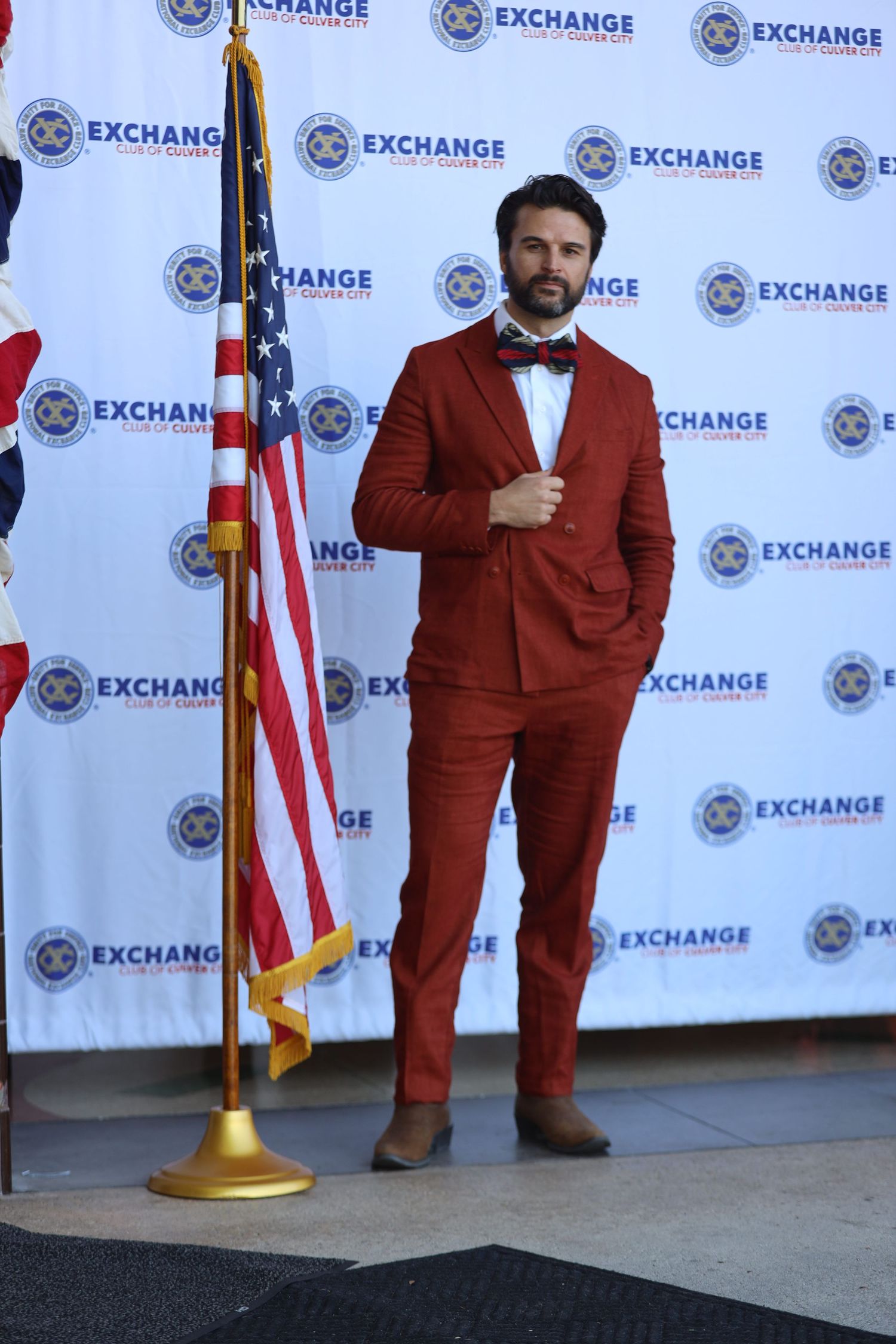Individual in red formal attire poses at Exchange event with flag display.