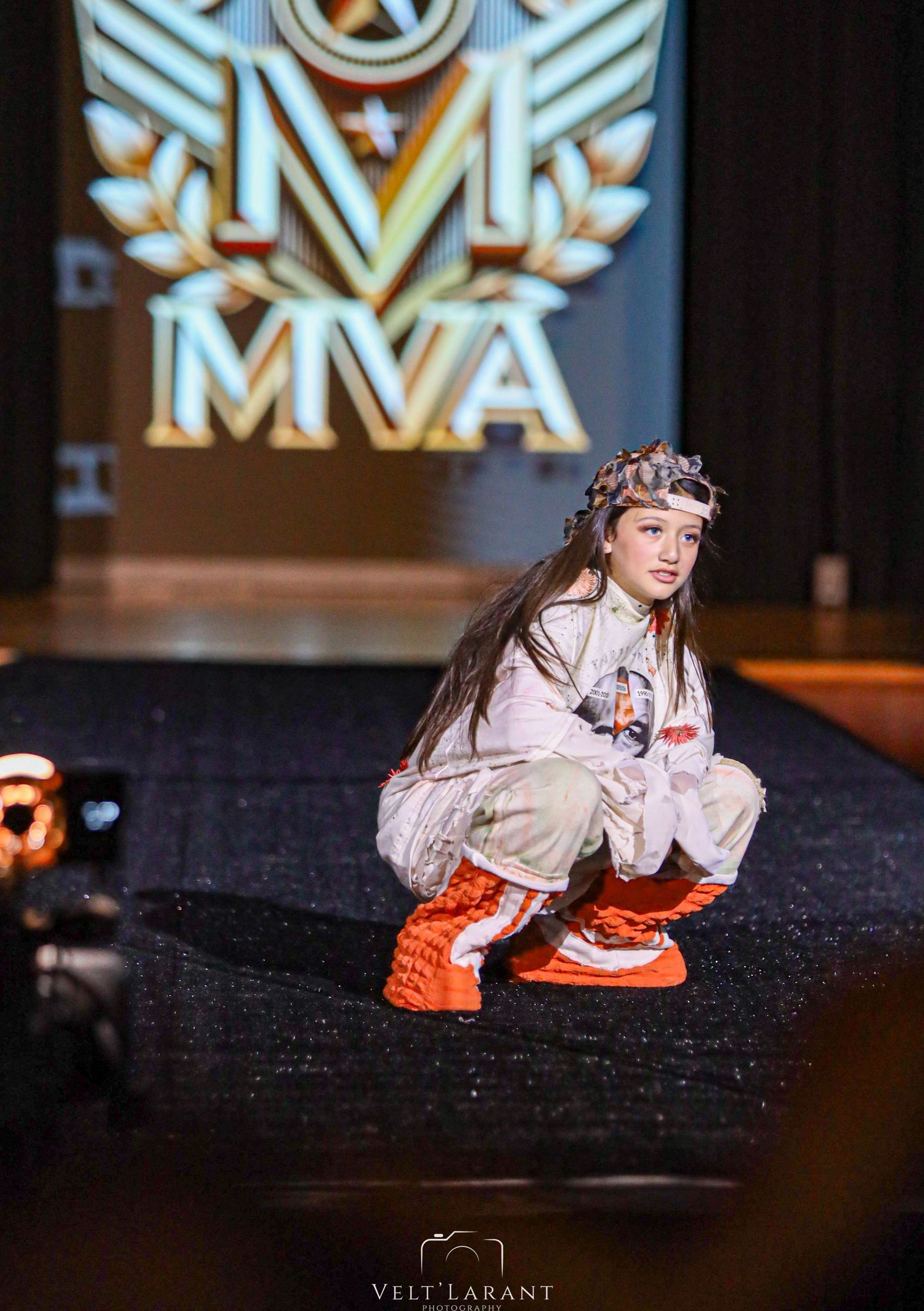 Street-style model in casual outfit crouches on runway wearing bright orange sneakers.