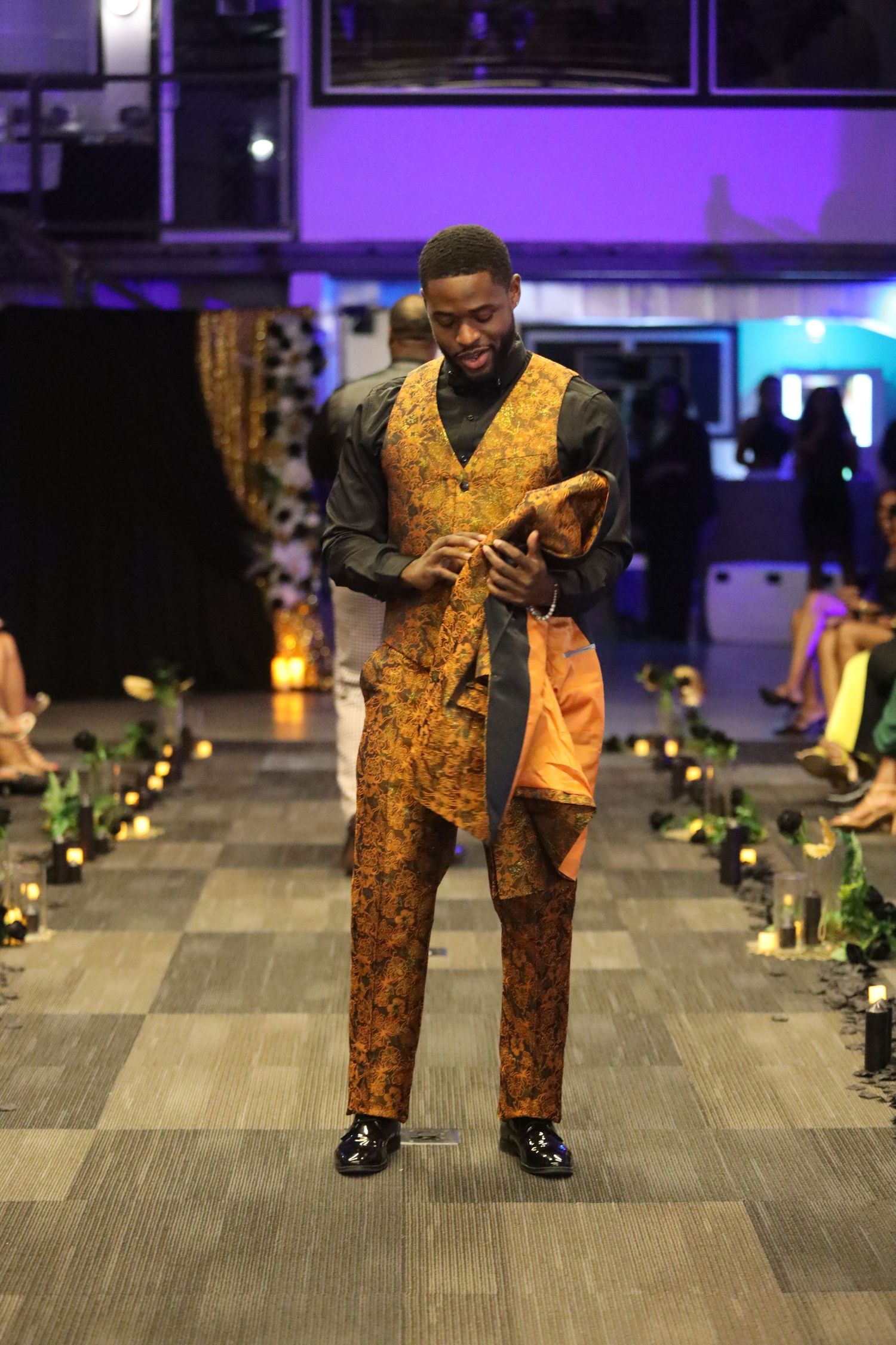 Gold brocade vest and pants ensemble modeled on runway with purple lighting.