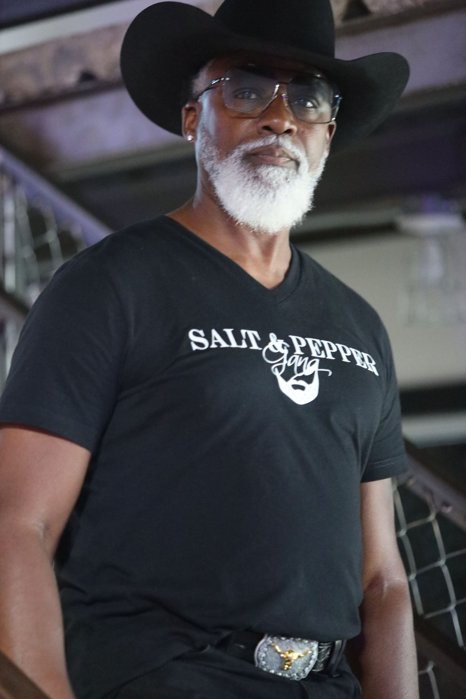 Person wearing black Salt & Pepper t-shirt and cowboy hat in dimly lit space.