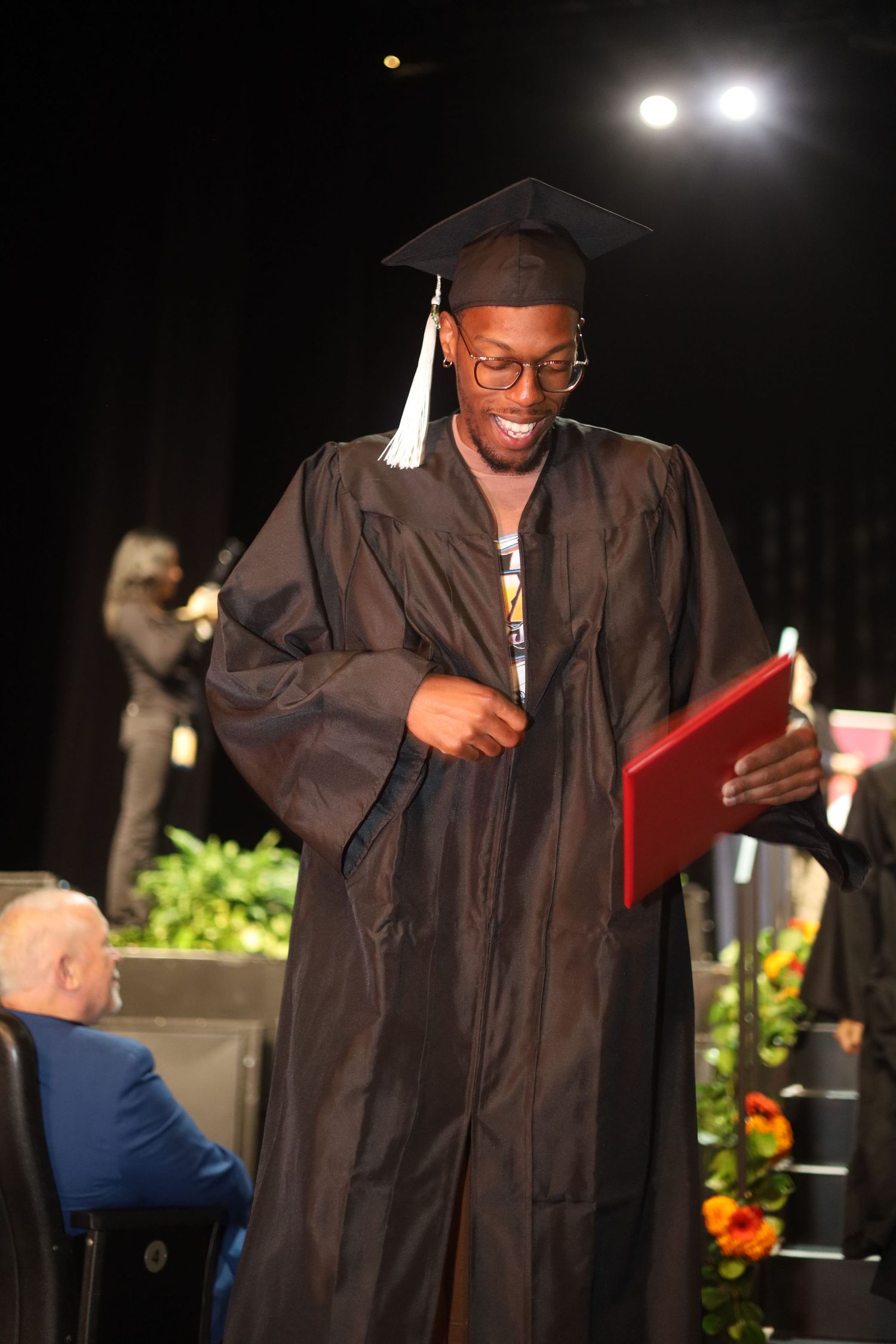 Graduate in black cap and gown smiling while receiving diploma on stage.