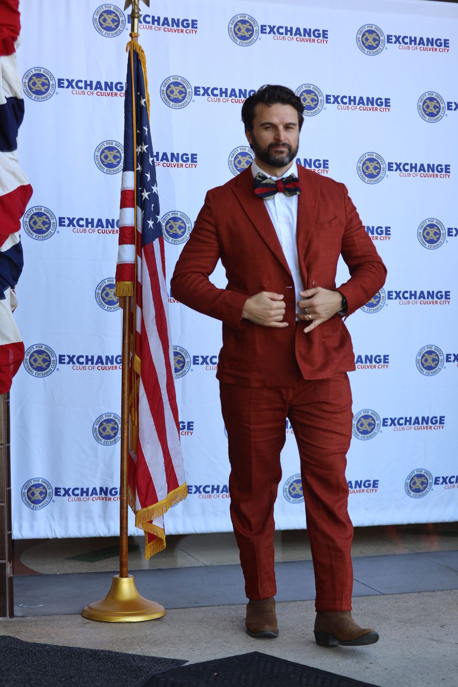 Individual poses in red formal suit at Exchange event with American flag display.