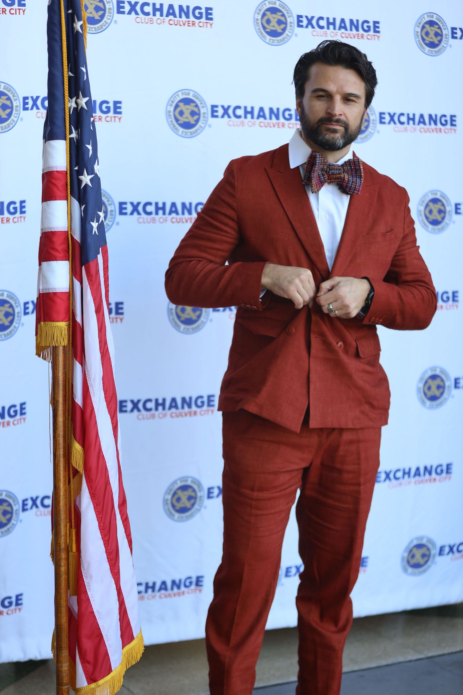 Person in a bright red suit poses against backdrop with Exchange logos and American flags.