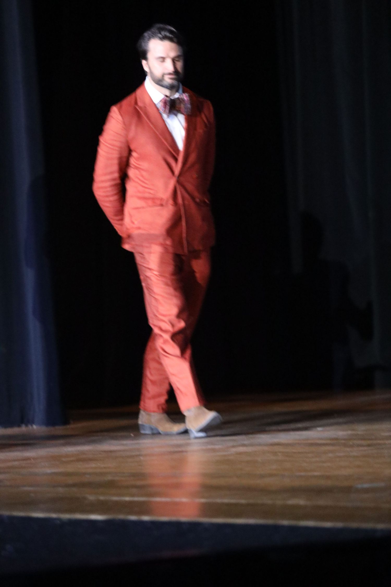 Person in a bright red suit walks across a dimly lit stage.