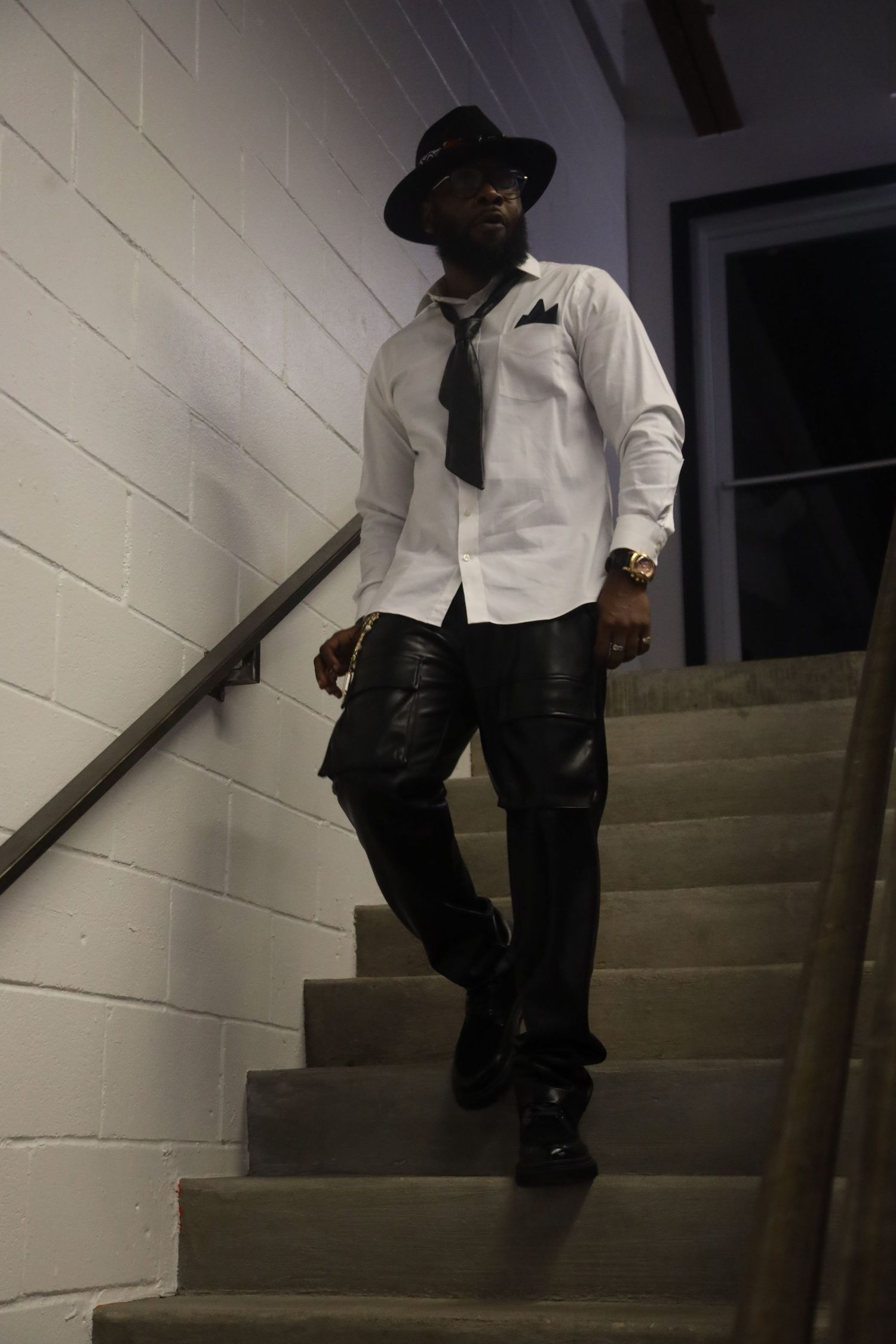 Person in white shirt and dark hat descending concrete stairs in dimly lit space.