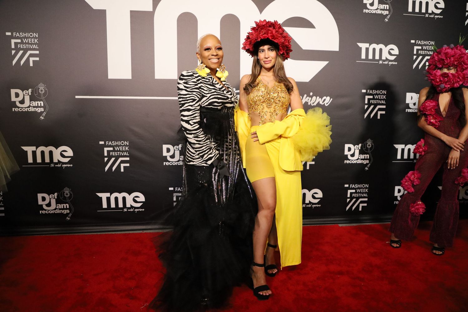 Fashion show attendees in elegant attire pose for photos on red carpet with TME branding.