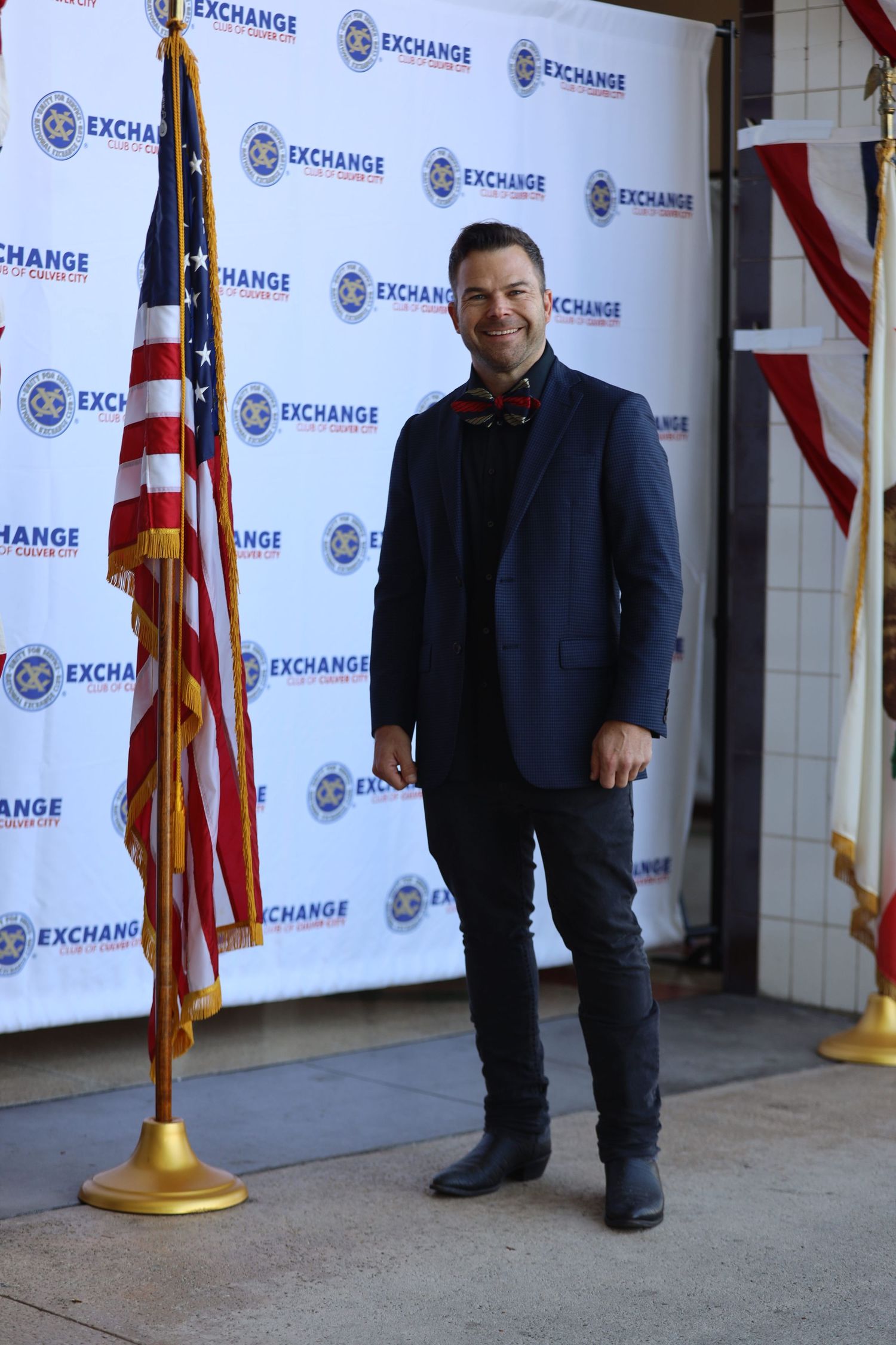 Person in navy blazer stands before promotional backdrop with flags.