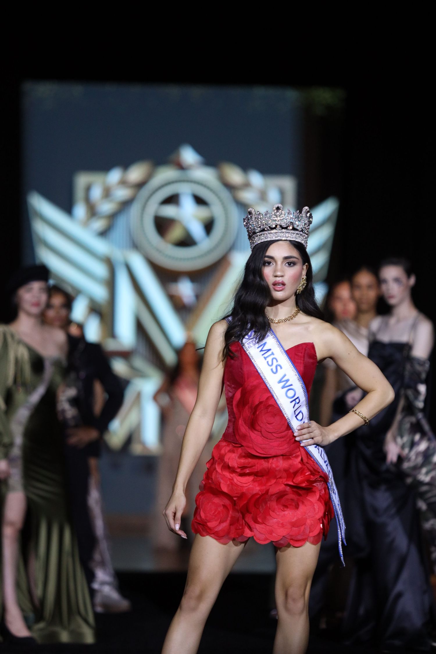 A beauty pageant winner in a short red dress and crown poses confidently on the runway.