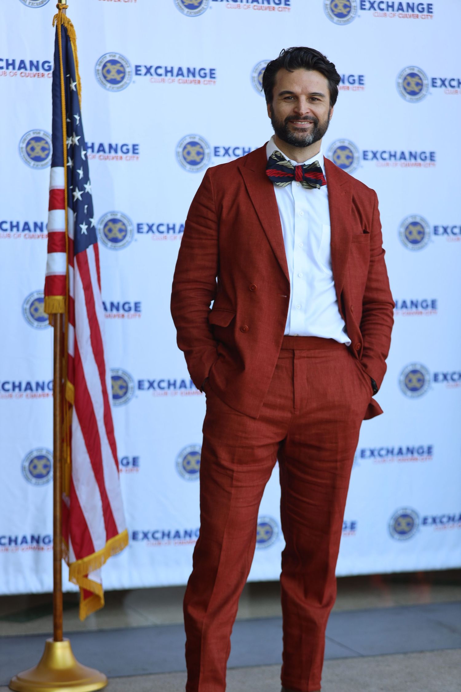 Figure in maroon suit and bowtie stands professionally at Exchange event.