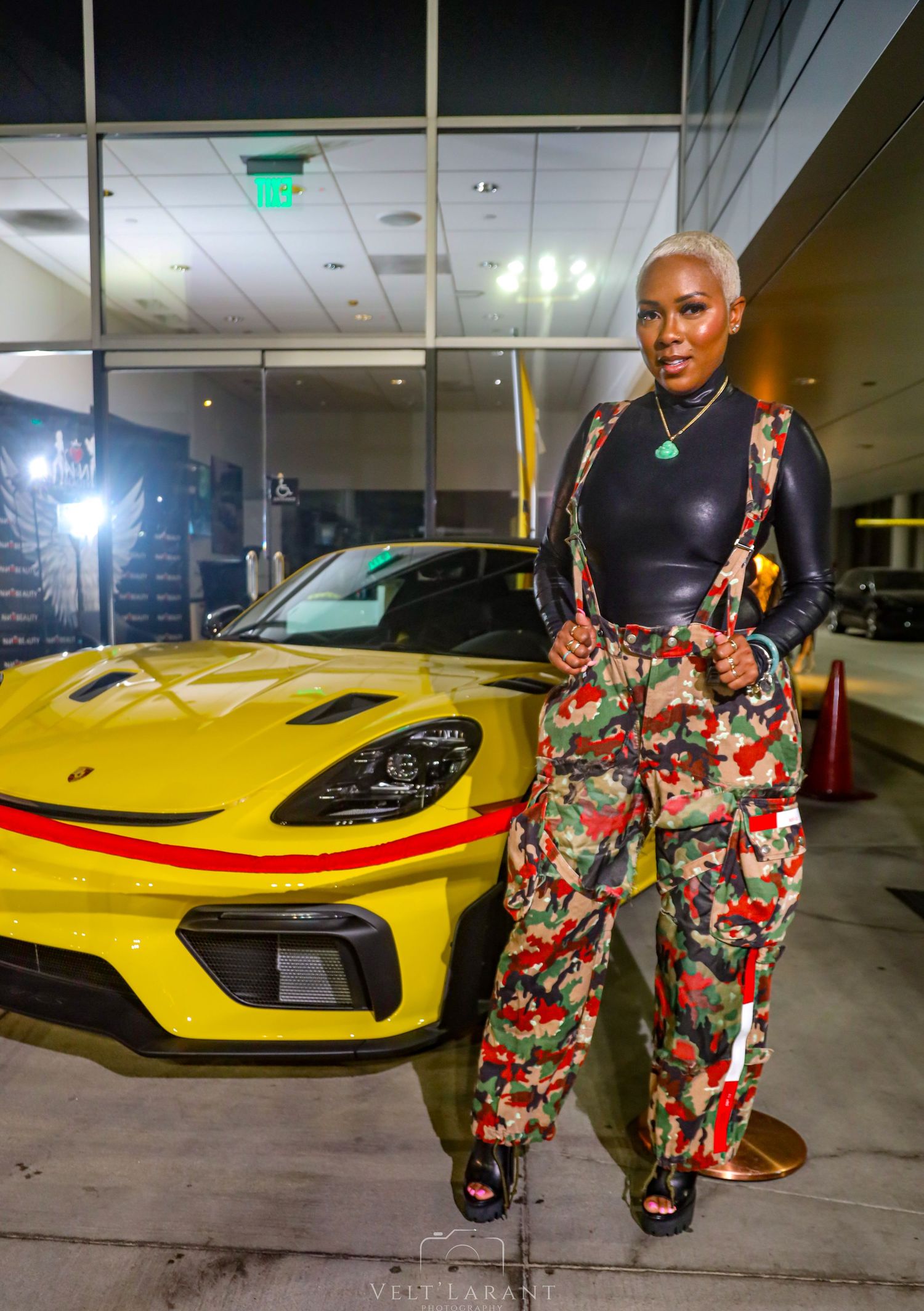 Stylish model poses next to a bright yellow Porsche sports car in a modern indoor setting.