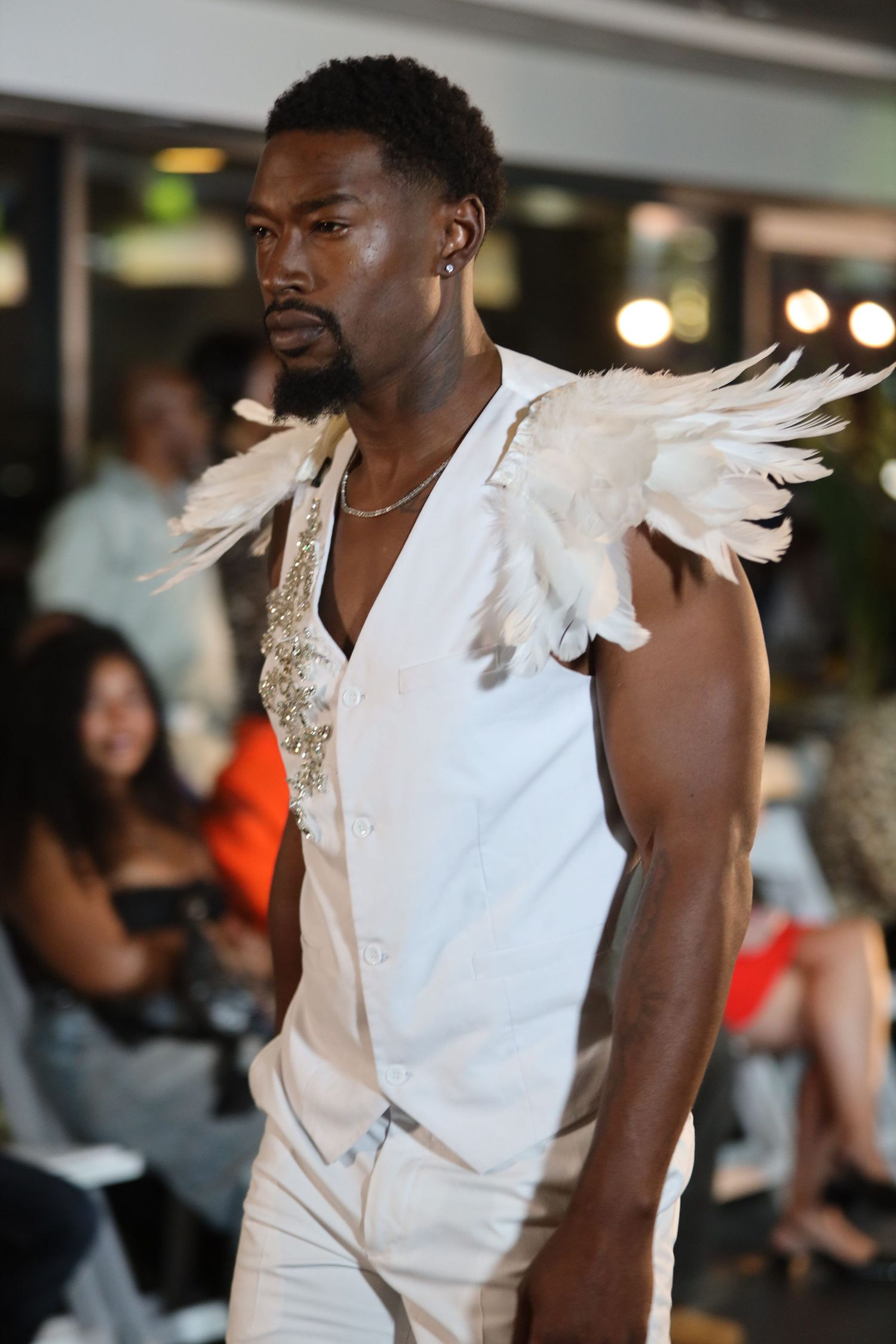 Fashion model showcases white avant-garde outfit with feather details on catwalk.