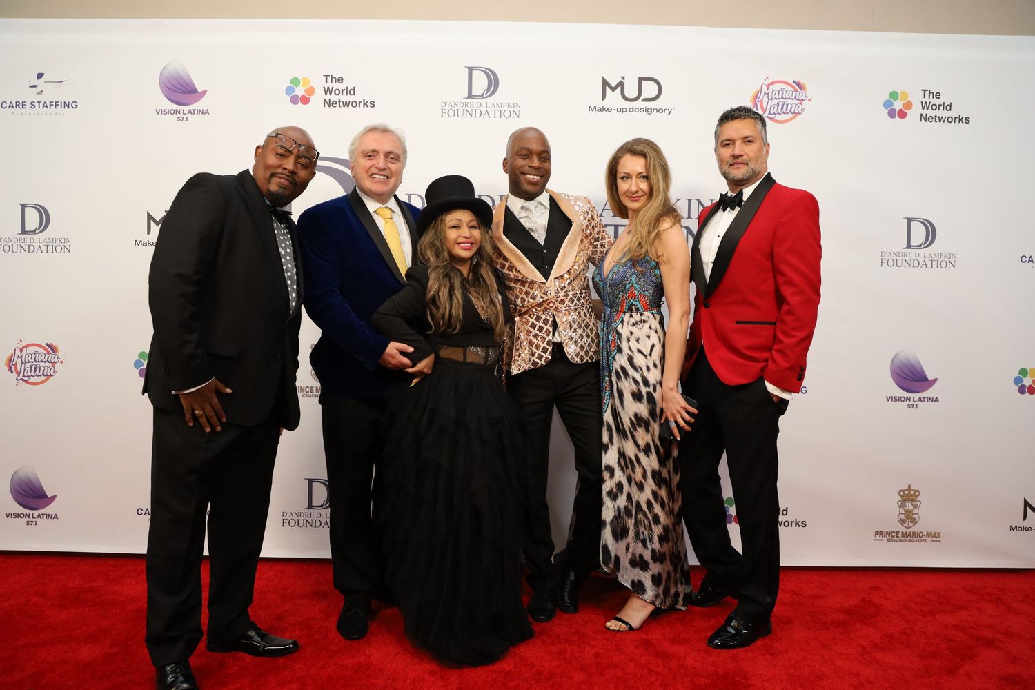 Group photo of elegantly dressed attendees posing together on red carpet at formal event.