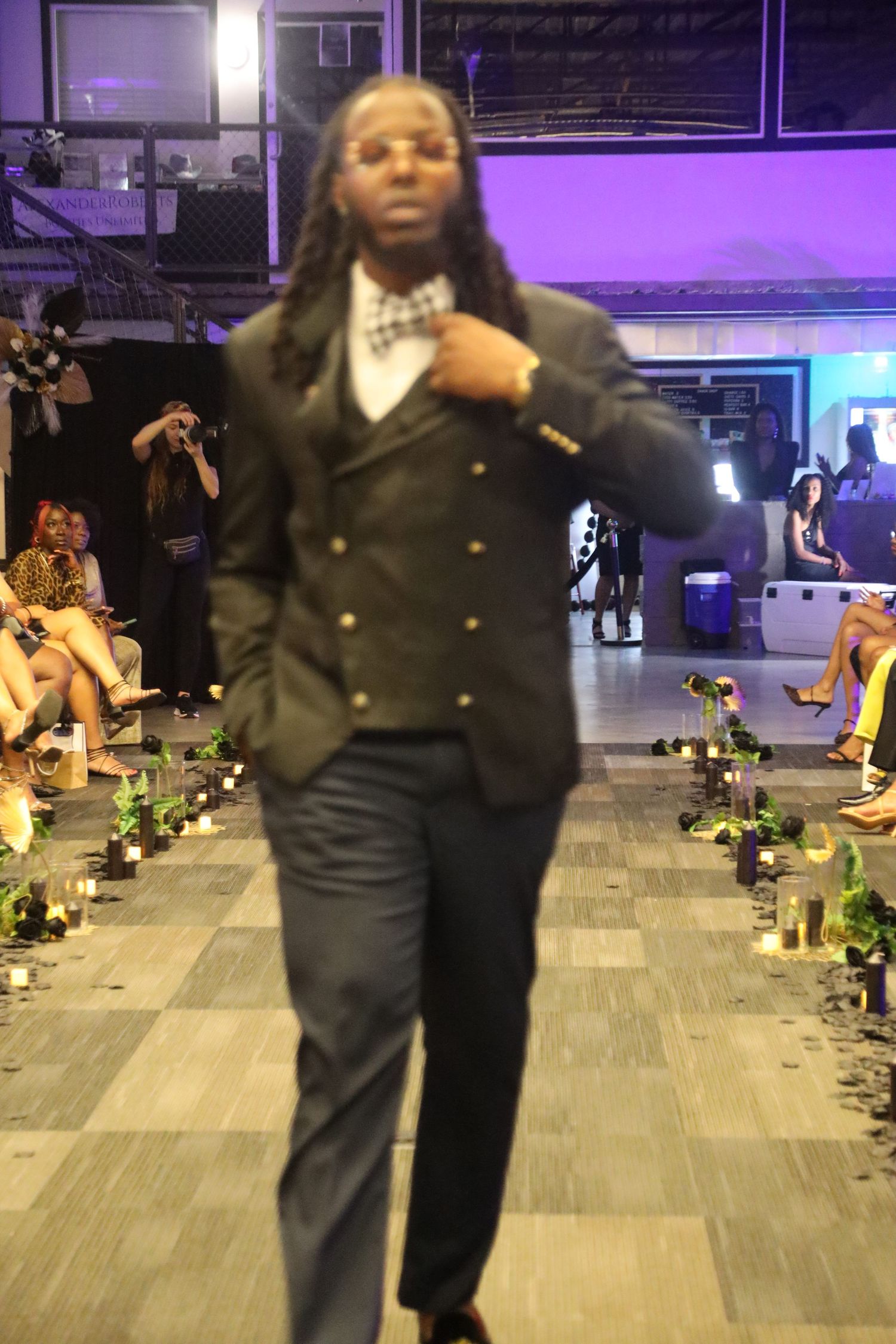 Figure in dark formal wear walking across tiled floor with purple ambient lighting.