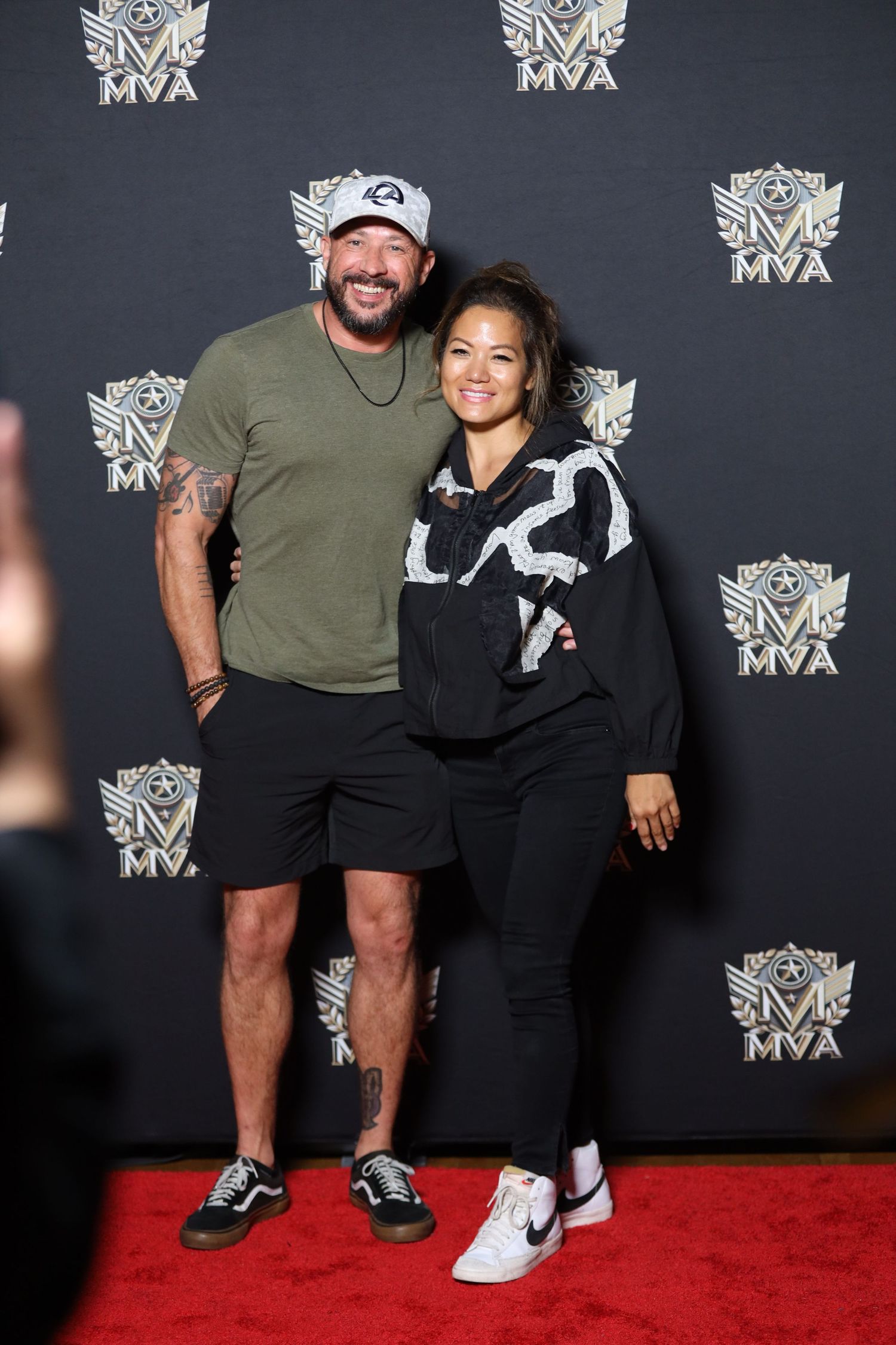 Two people pose together at an event with MVA logos in the background on a red carpet.