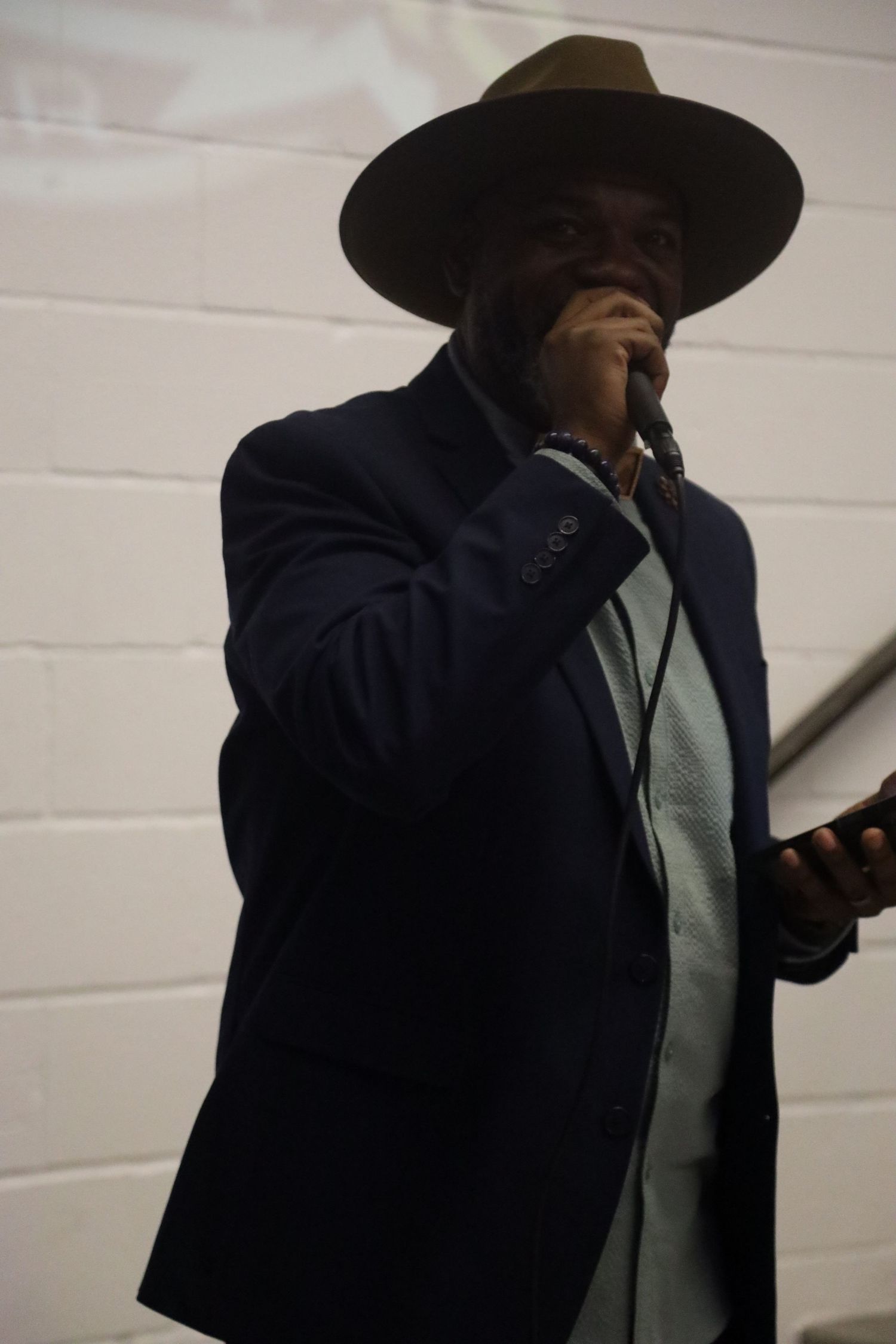 Figure in dark suit and wide-brimmed hat moving through dimly lit corridor.