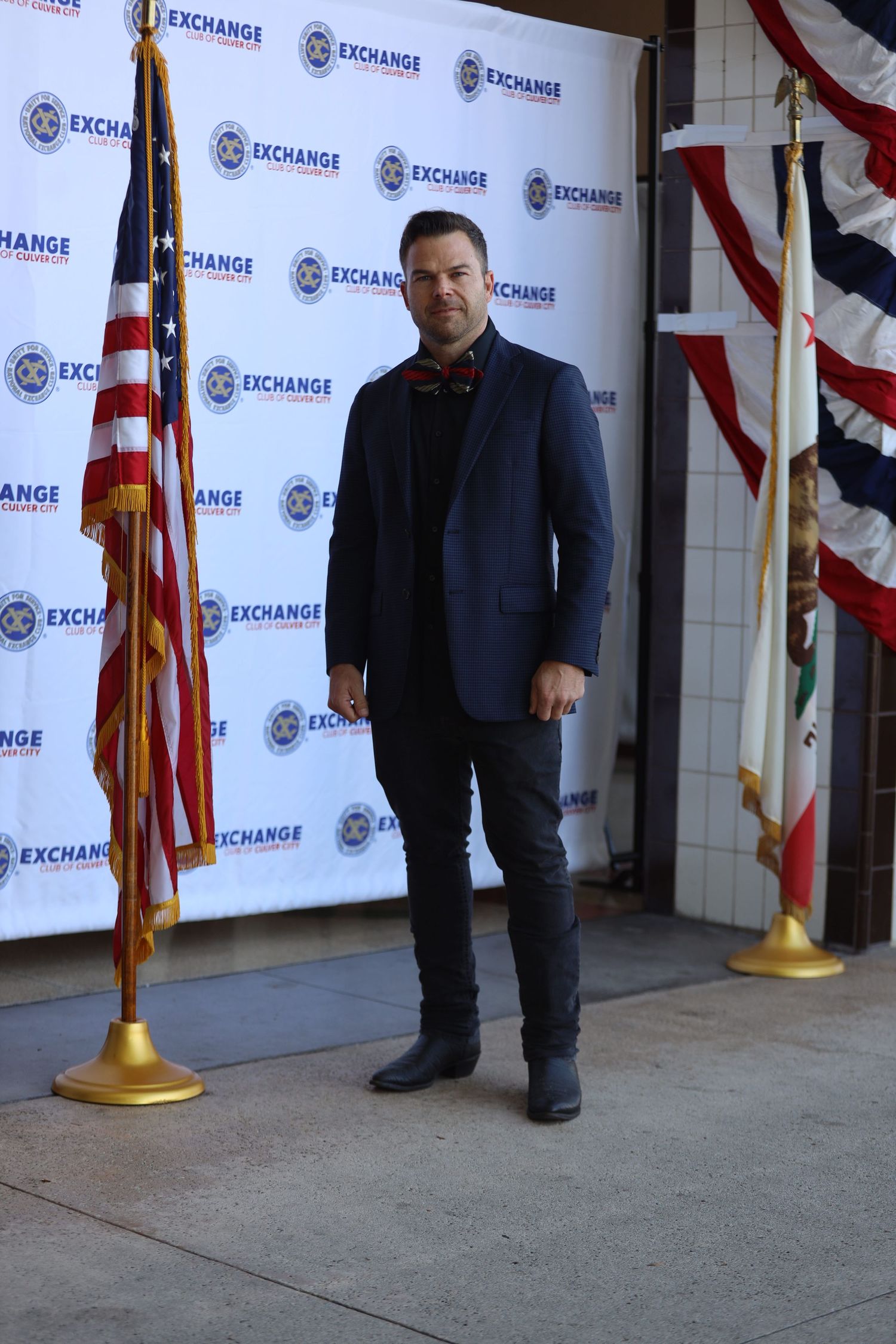 Individual poses in formal attire against backdrop with American flags and Exchange logos.