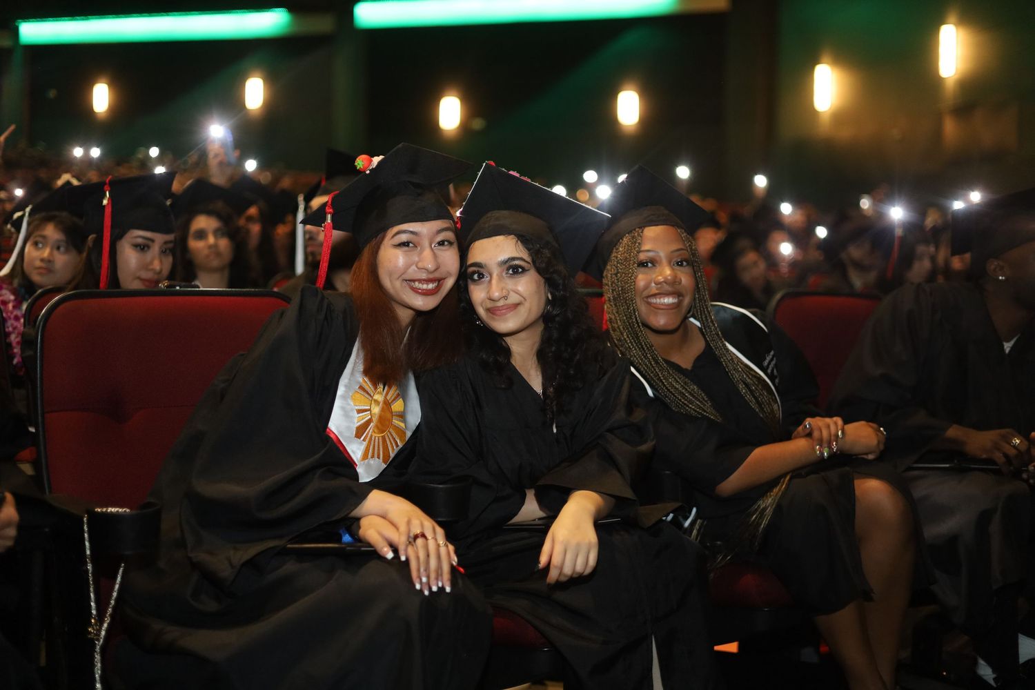 Students in graduation attire celebrating under green lighting.