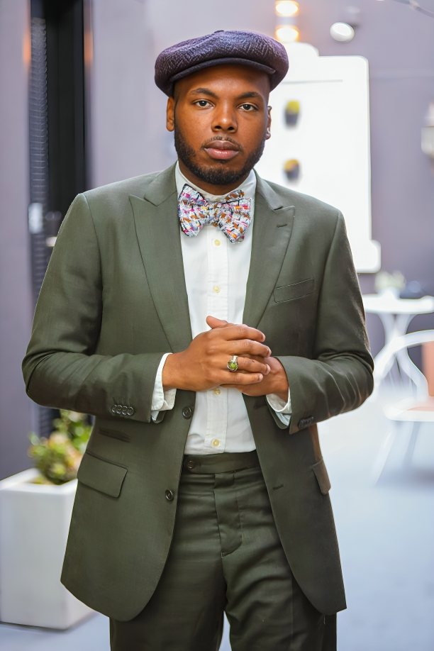 Stylish ensemble featuring olive green suit, floral bowtie and flat cap.