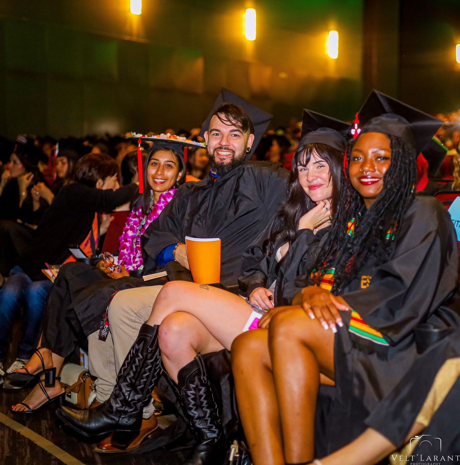Group of graduates celebrating together at commencement ceremony with festive lighting.
