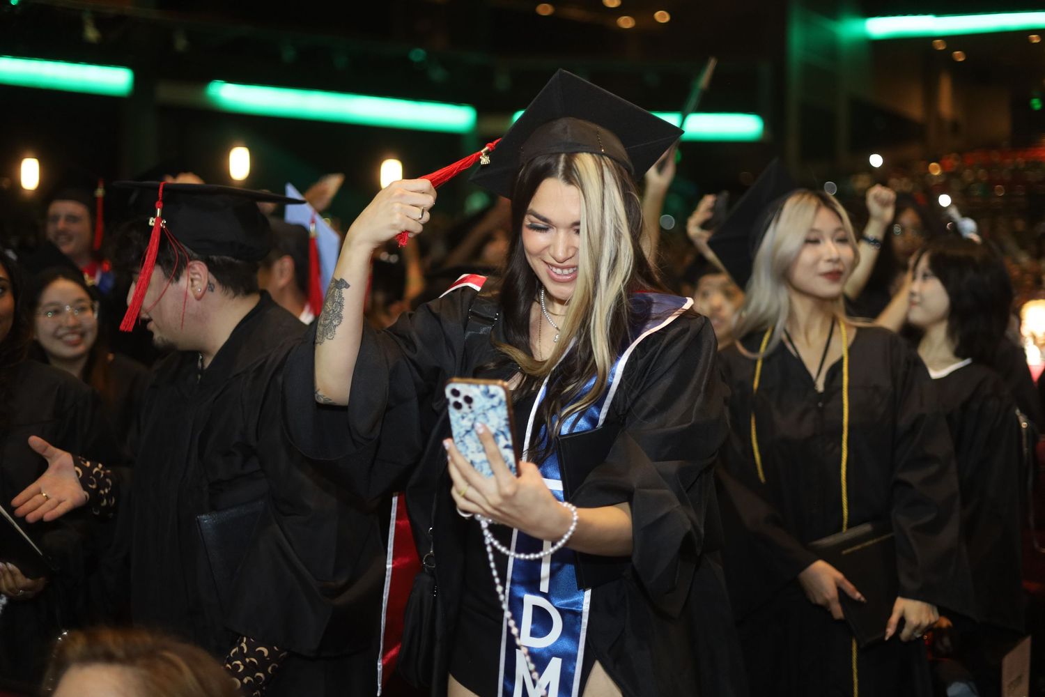 Graduates celebrating with raised hands in a dimly lit auditorium.