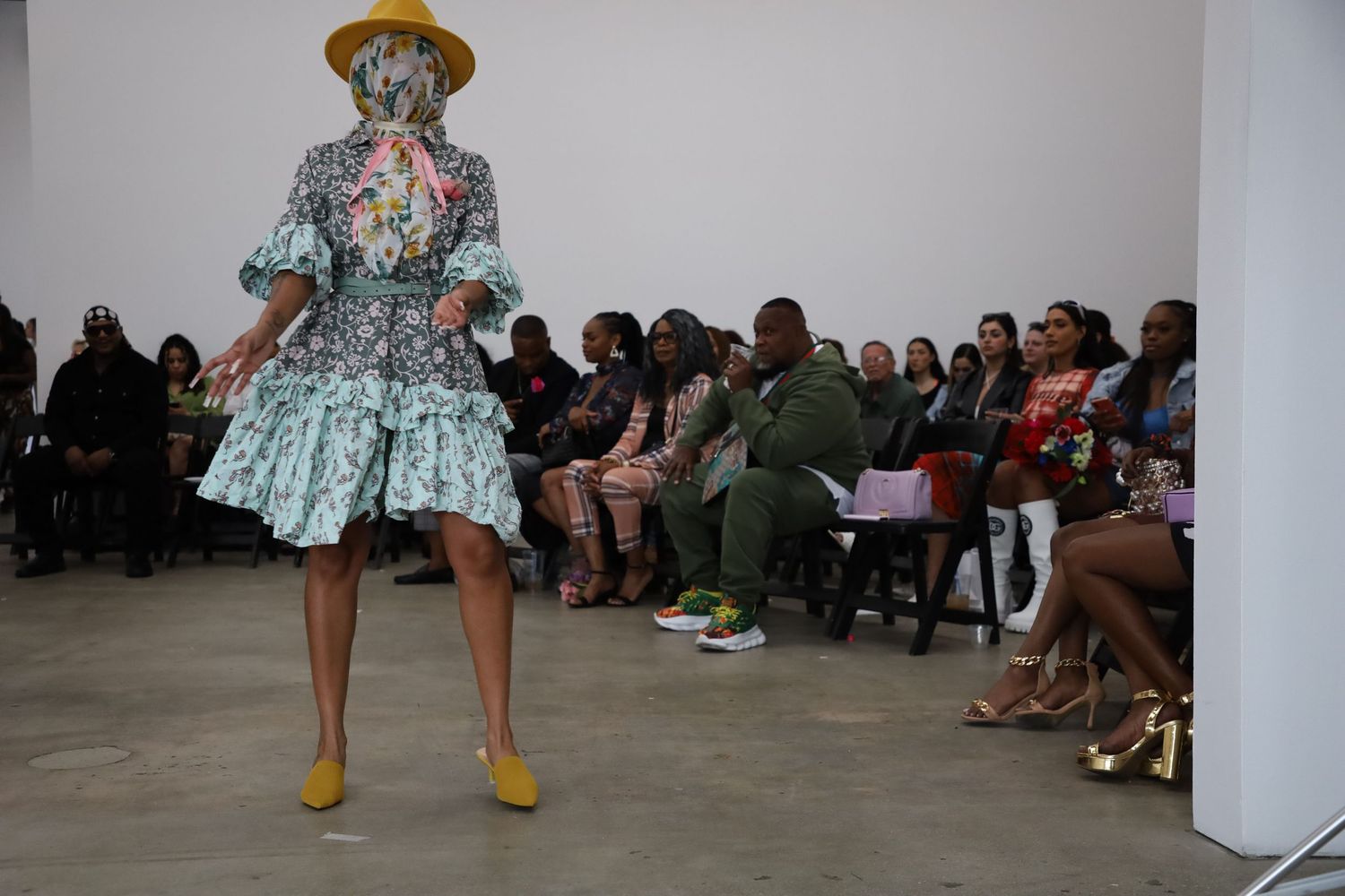 Yellow accessories complement floral dress during gallery fashion presentation.