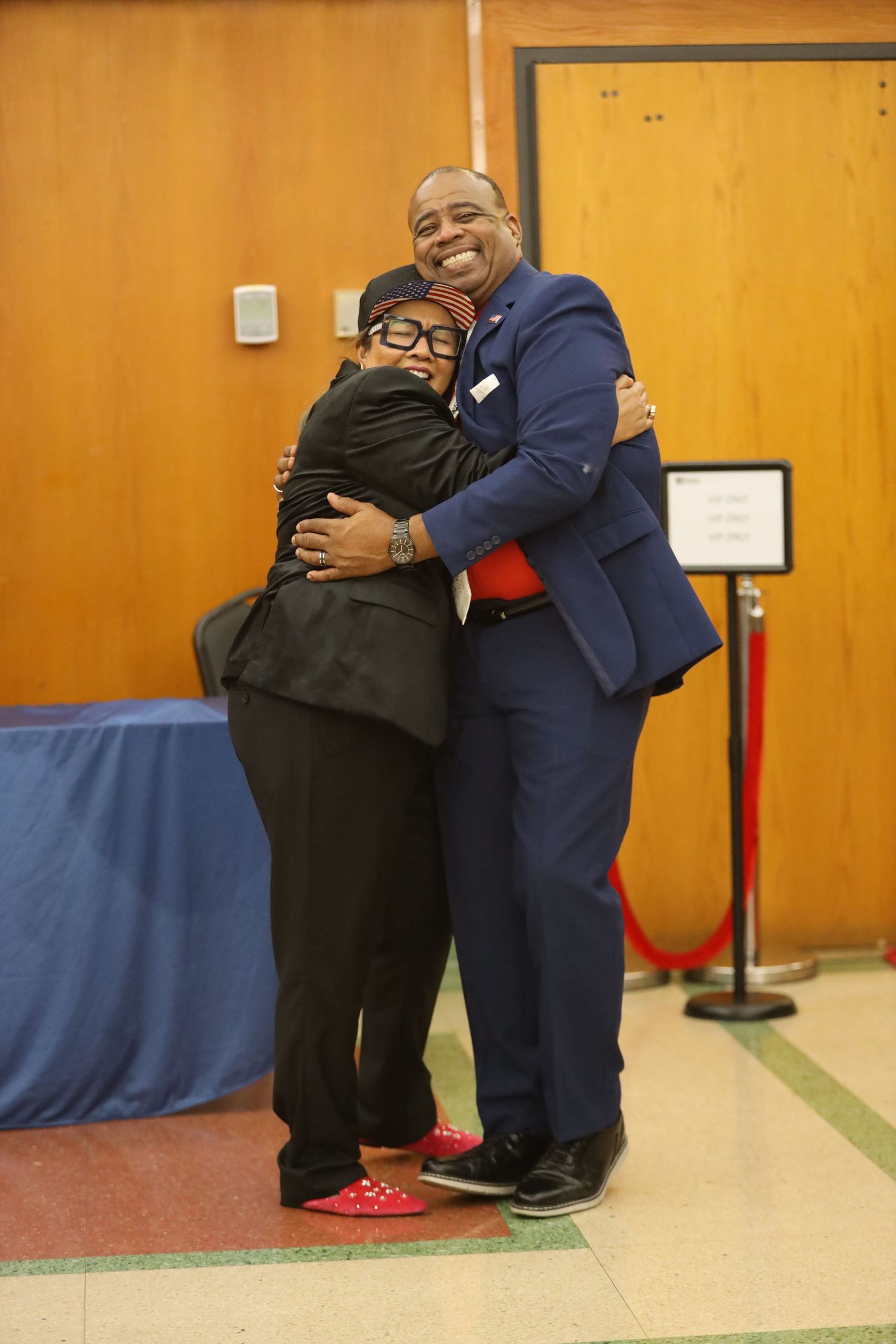Two people share a warm embrace while posing for a photo in an indoor venue.