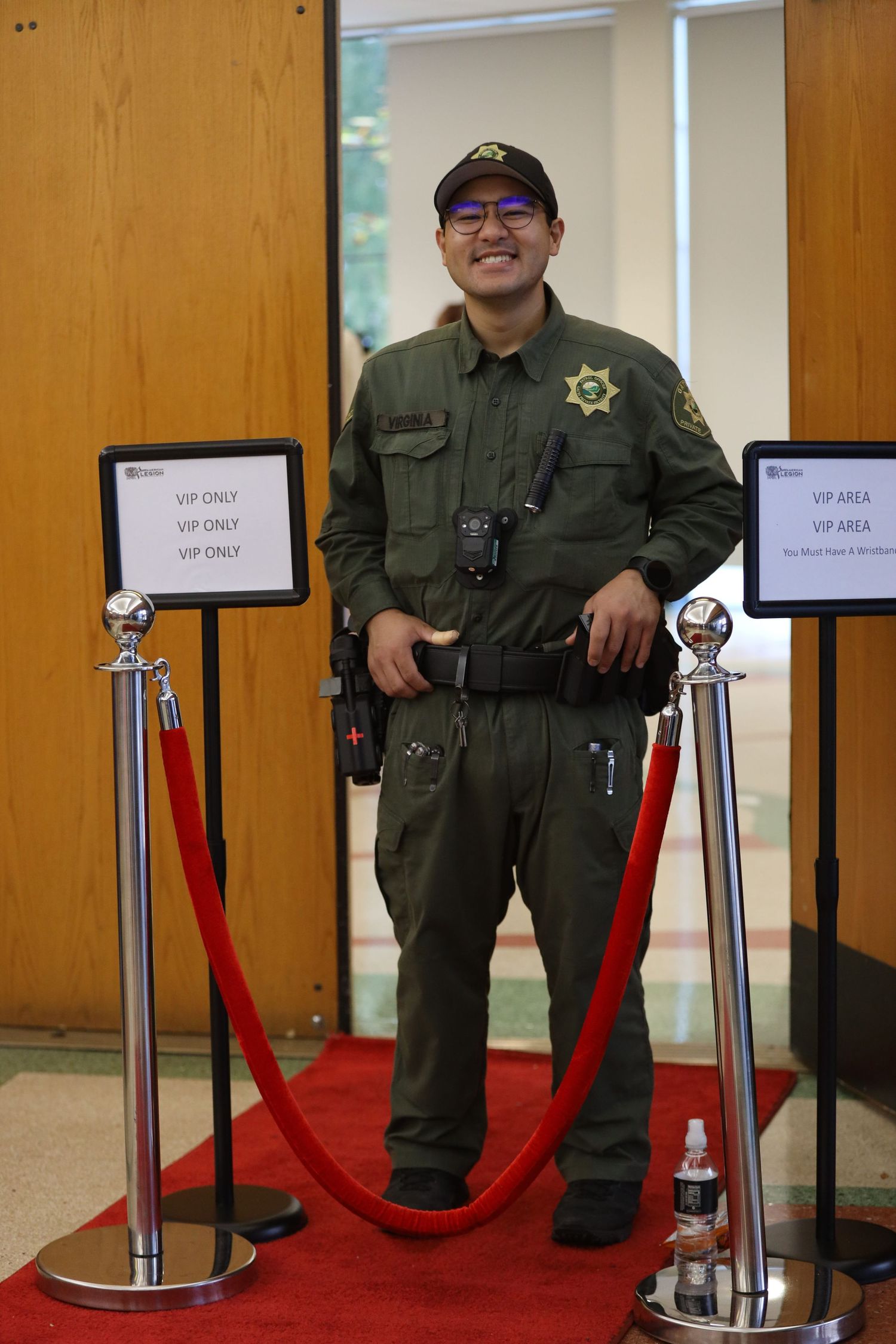 Security personnel in uniform stands behind red velvet ropes in an indoor venue.