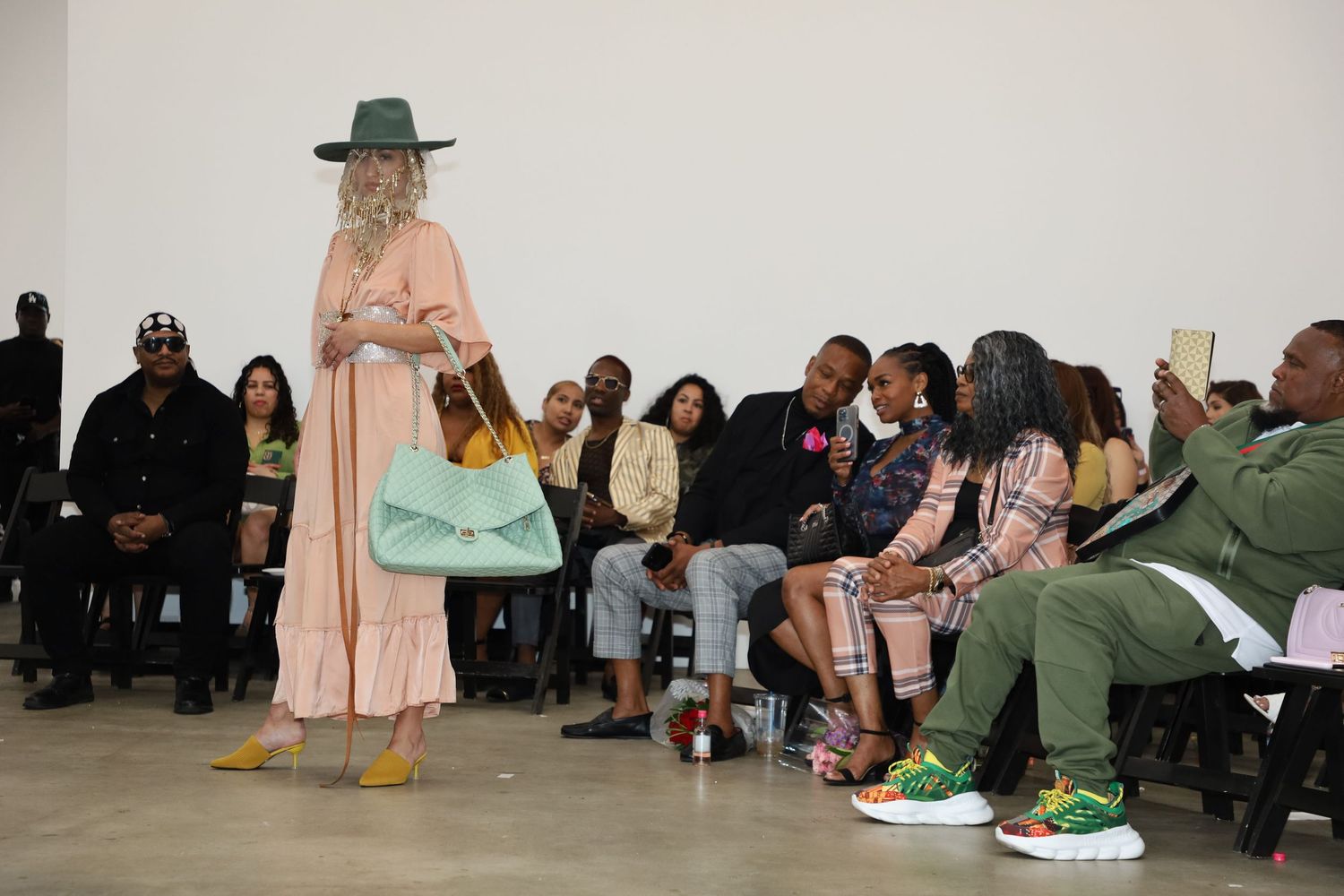 Fashion show featuring models in pastel outfits and hats with audience viewing the performance.