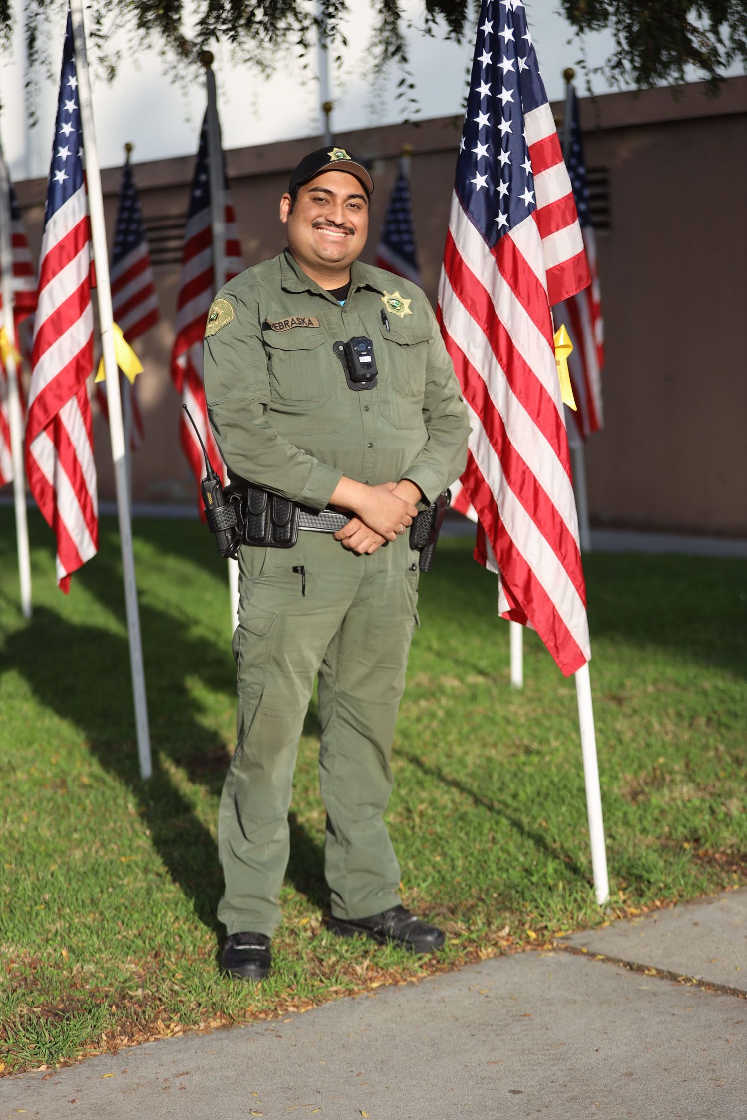 Law enforcement officers in uniform stand at attention near American flags on display.