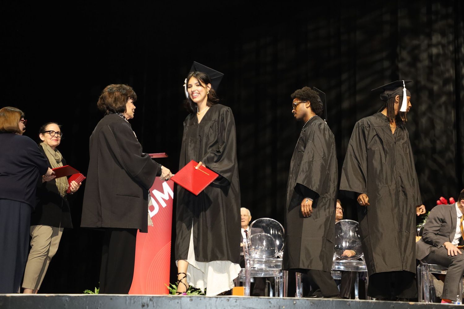 Students in graduation attire walk across stage during diploma presentation.