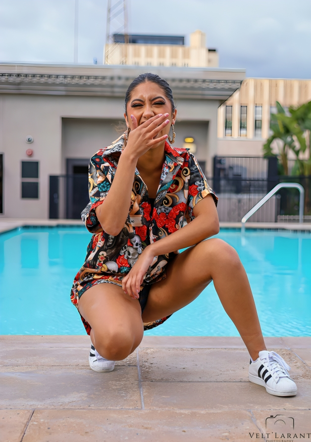 Model poses in floral print outfit by swimming pool with urban buildings in background.