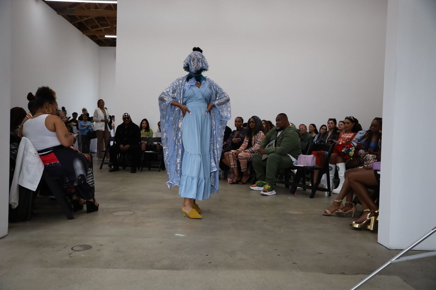 Models present spring fashion collection on industrial runway with seated audience.