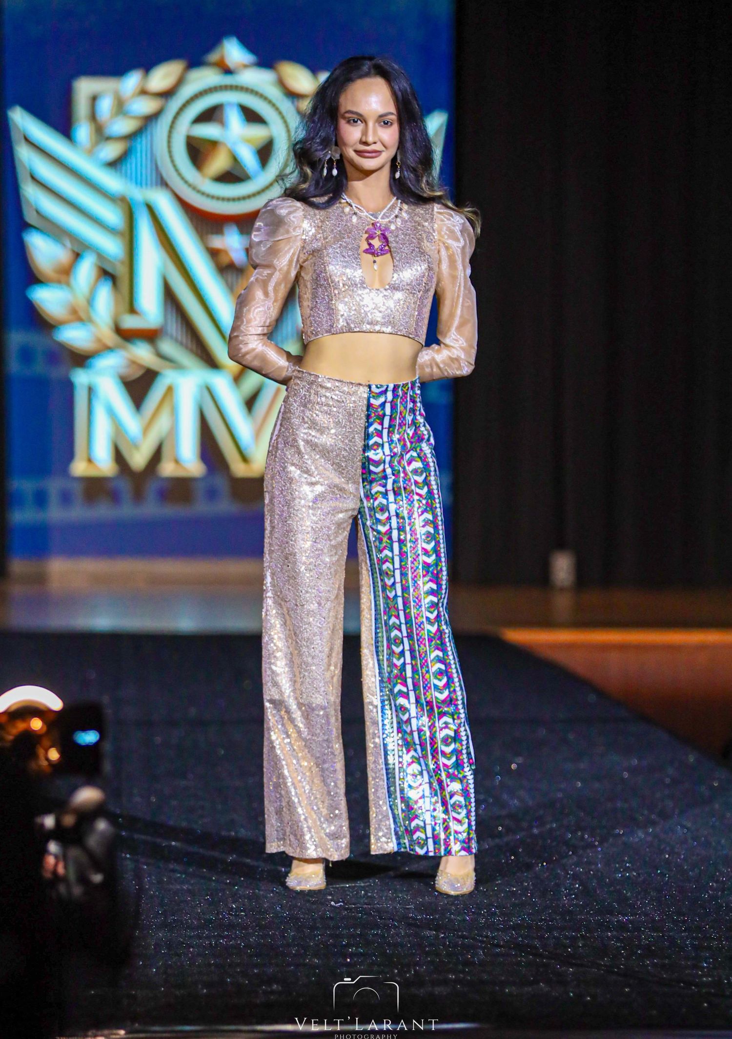 Model wears shimmering crop top with patterned wide-leg pants on fashion runway.