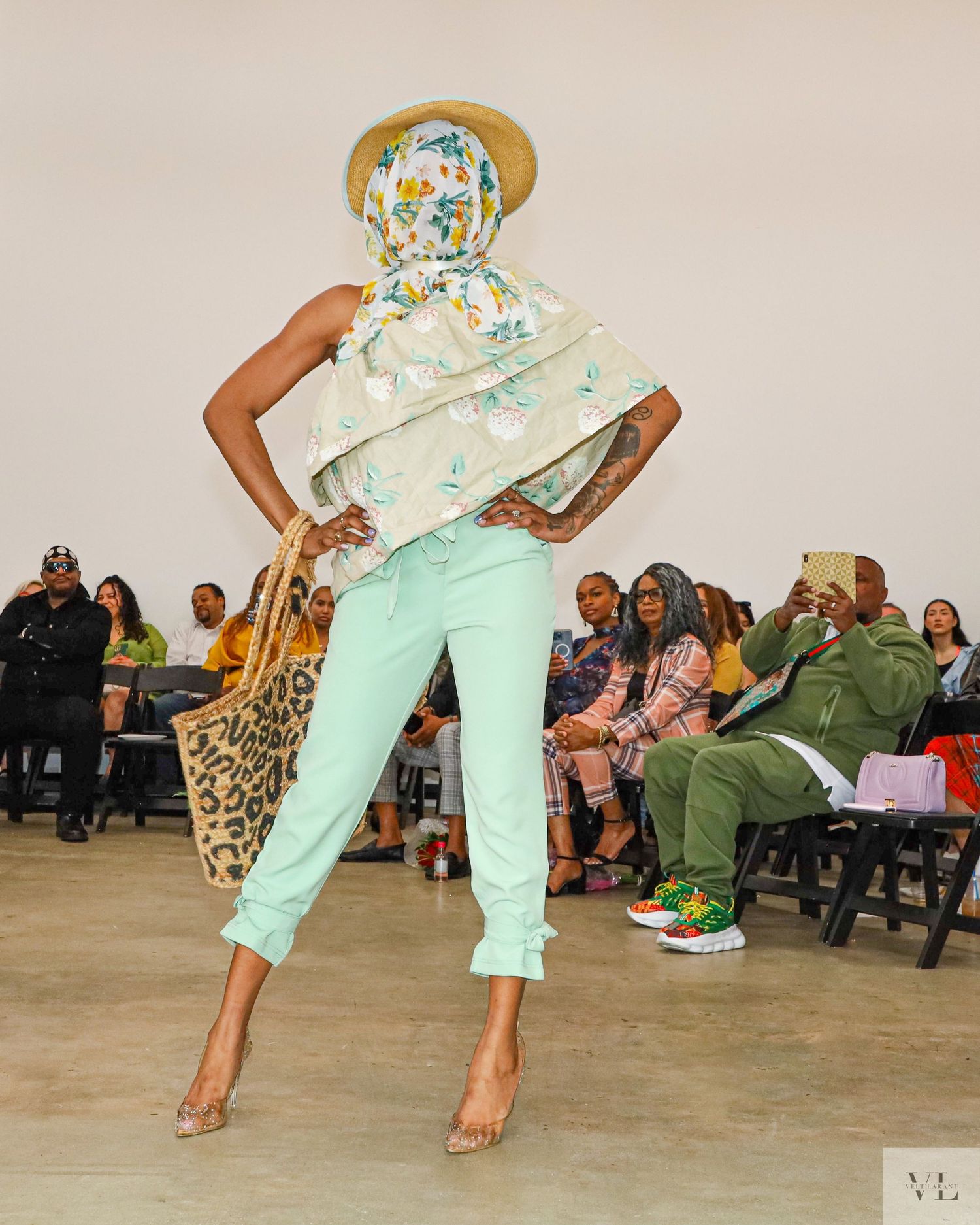 Energetic runway performance featuring mint green pants and floral print ensemble with audience seated.
