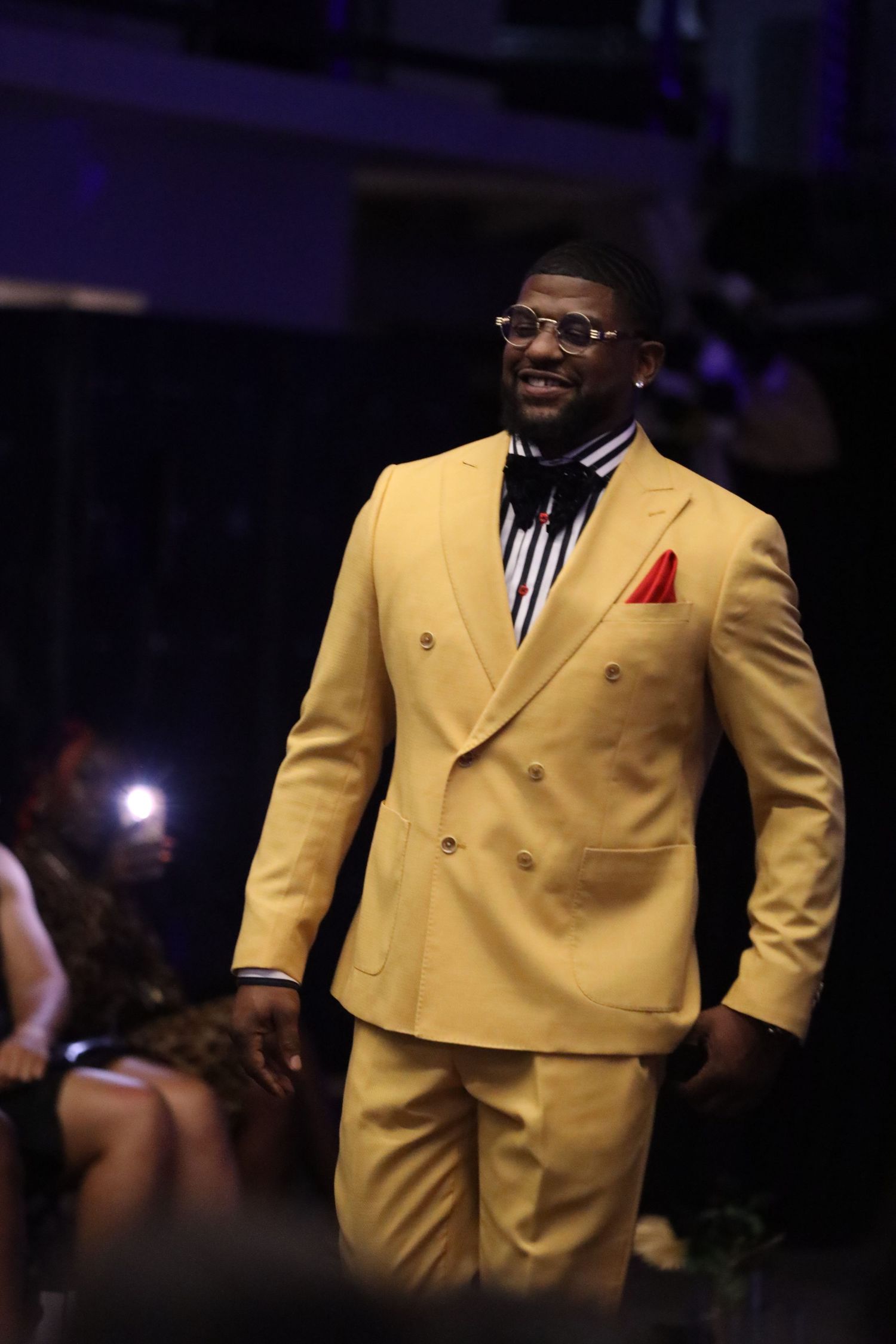 Person modeling yellow double-breasted suit on darkened runway.