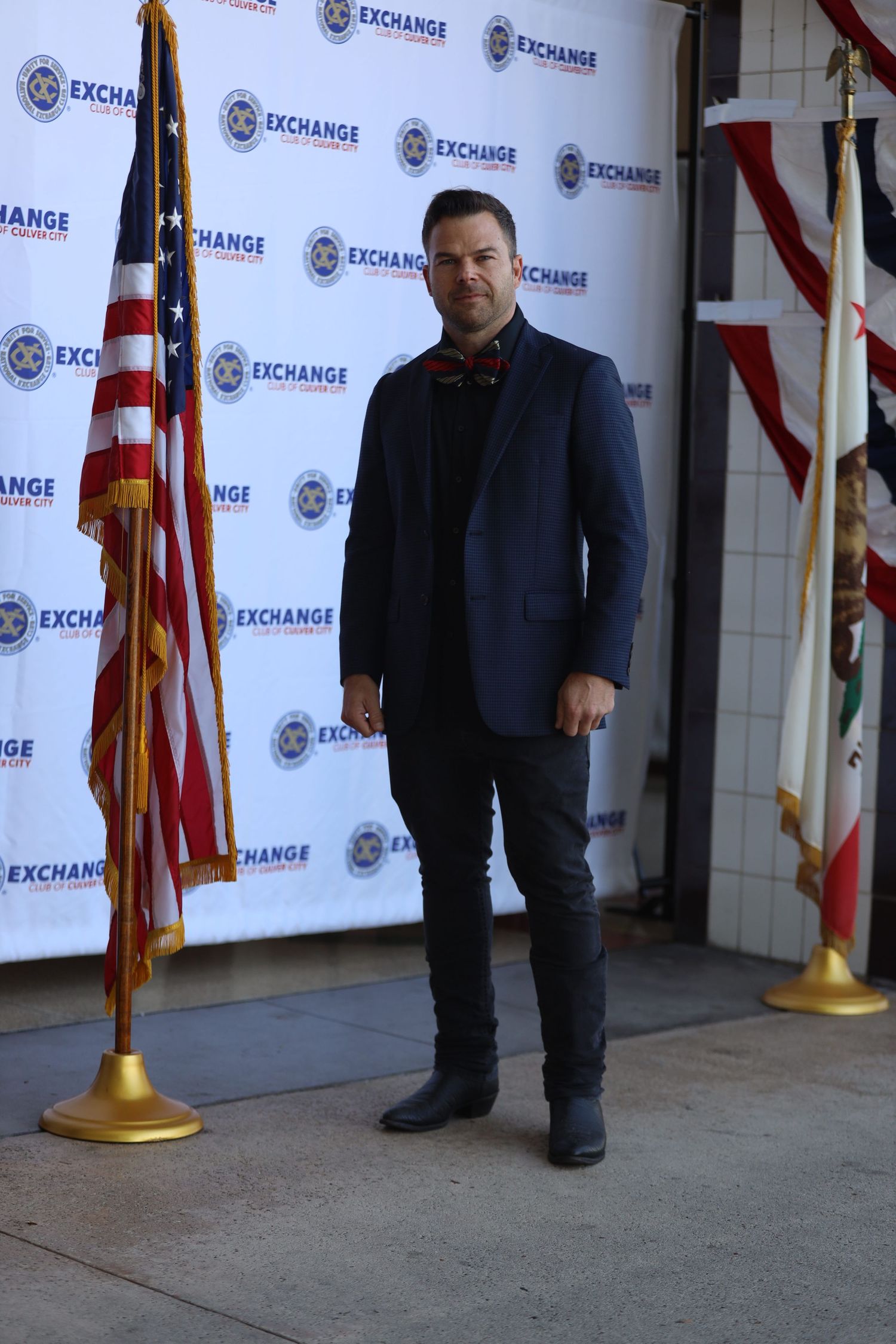 Individual stands on concrete floor against Exchange branded wall with flags.