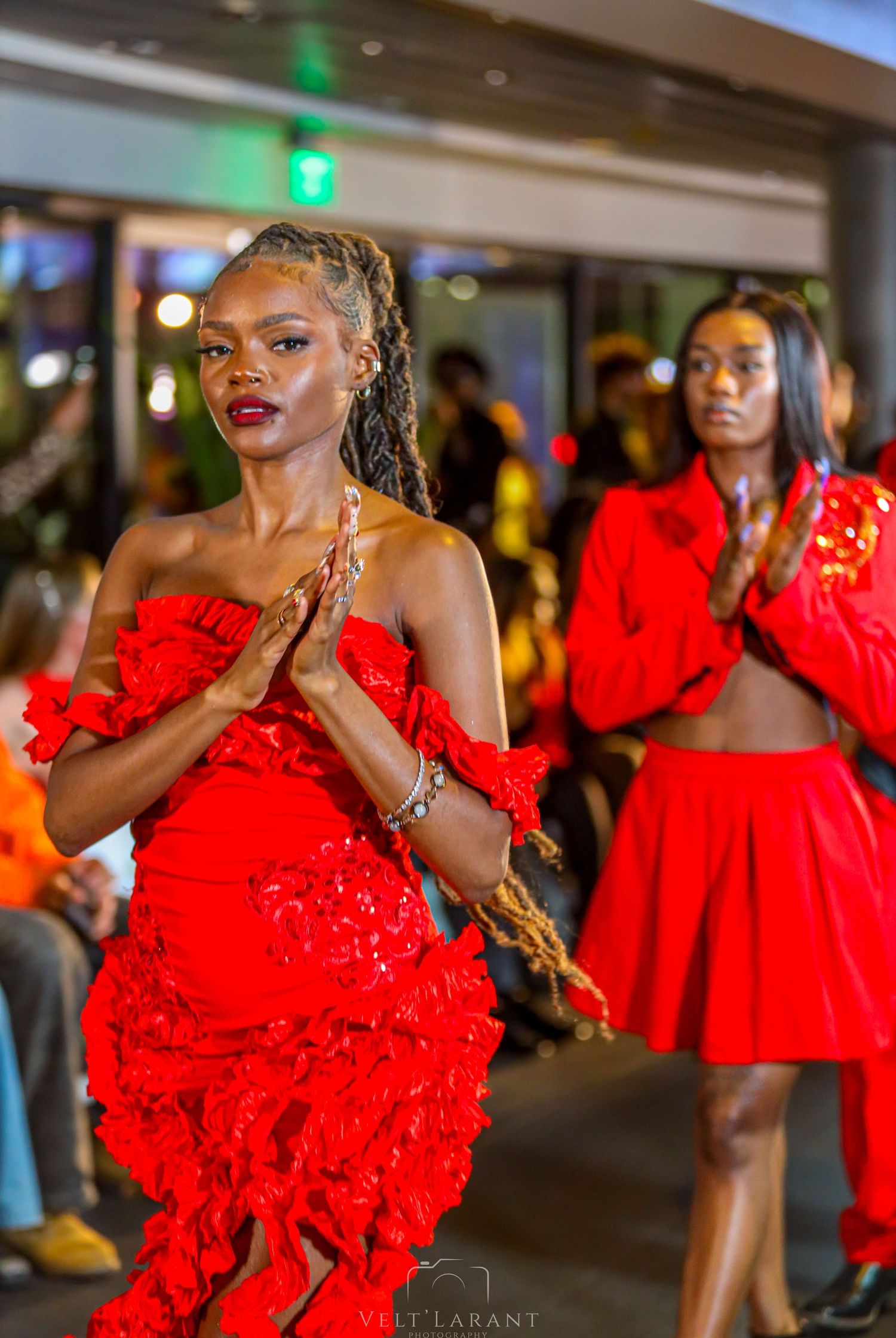 Models present collection of vibrant red dresses with dramatic ruffles at fashion event.