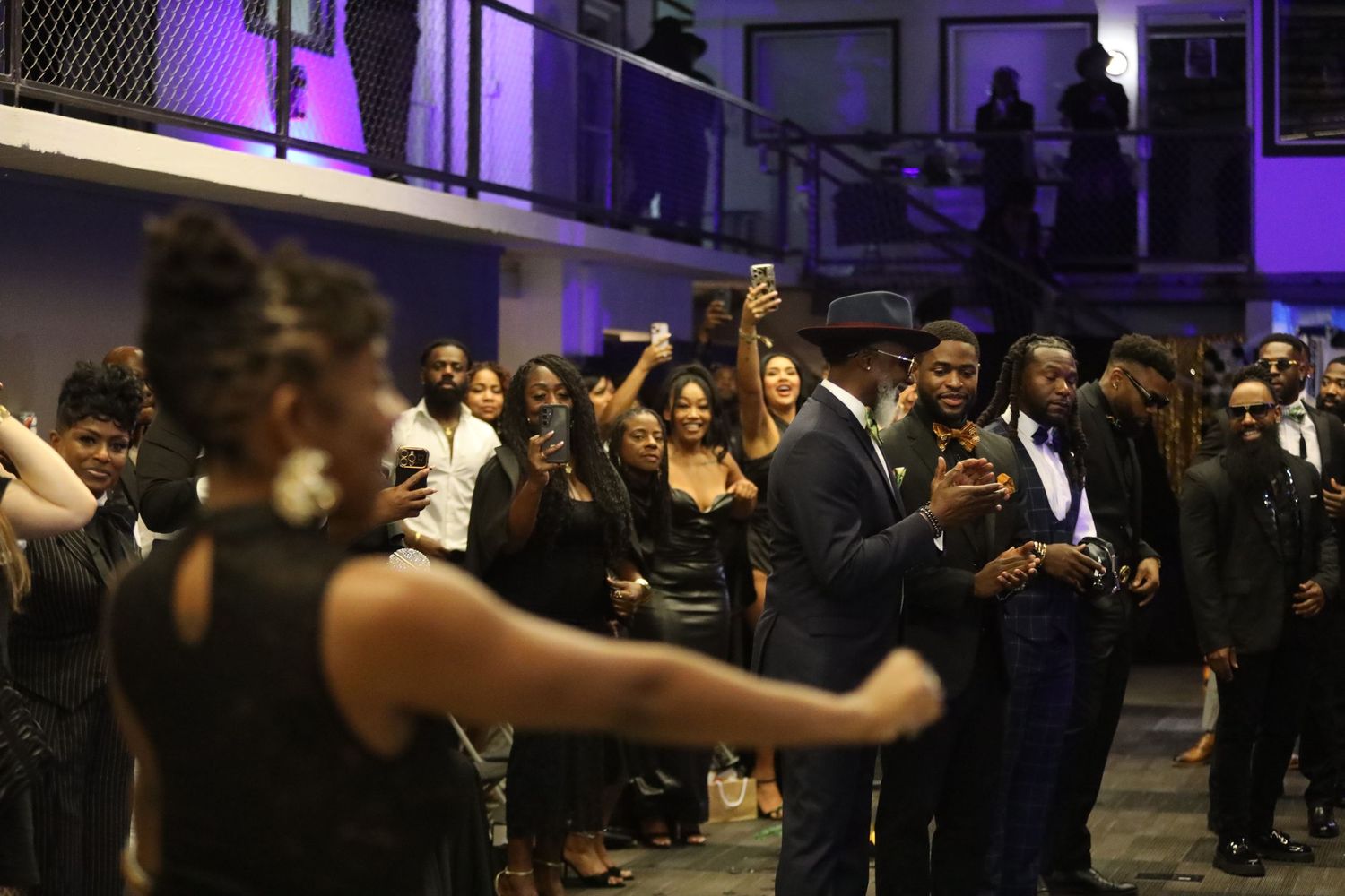 Crowd of attendees dancing and mingling at an elegant evening event with purple lighting.