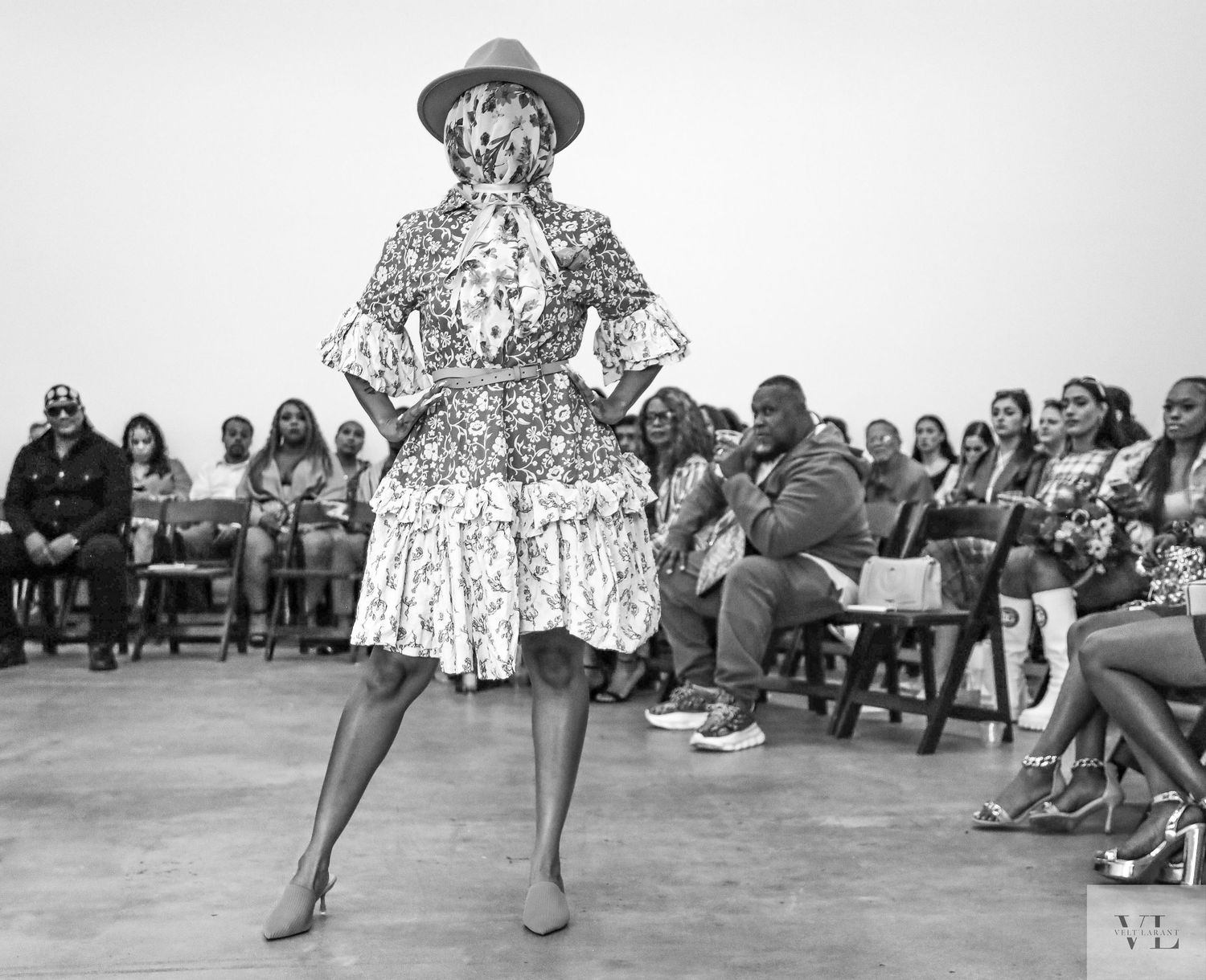 Fashion show audience watches models walk down a runway in a white industrial space.