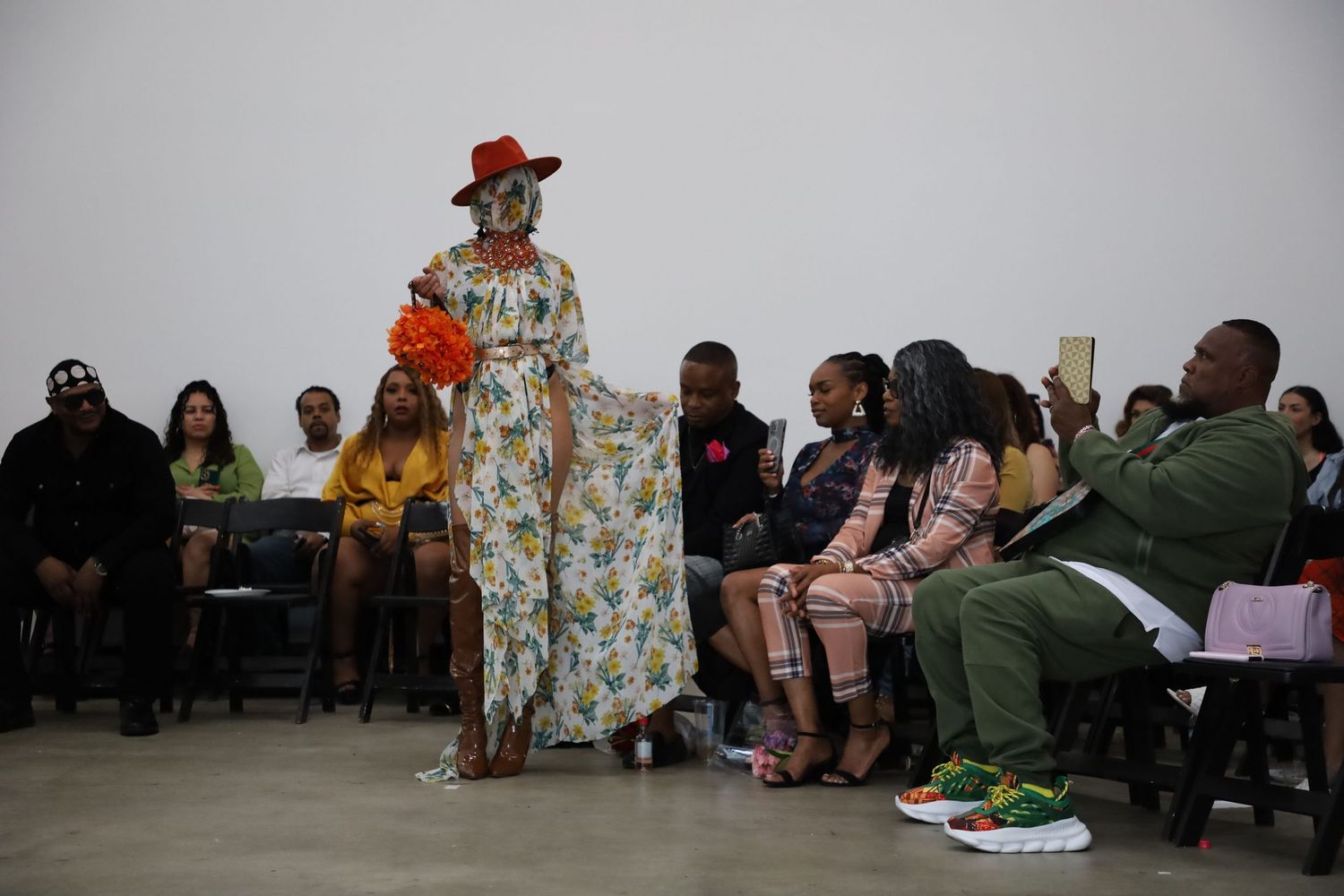 Fashion show featuring red hat and floral print designs with audience viewing from sides.