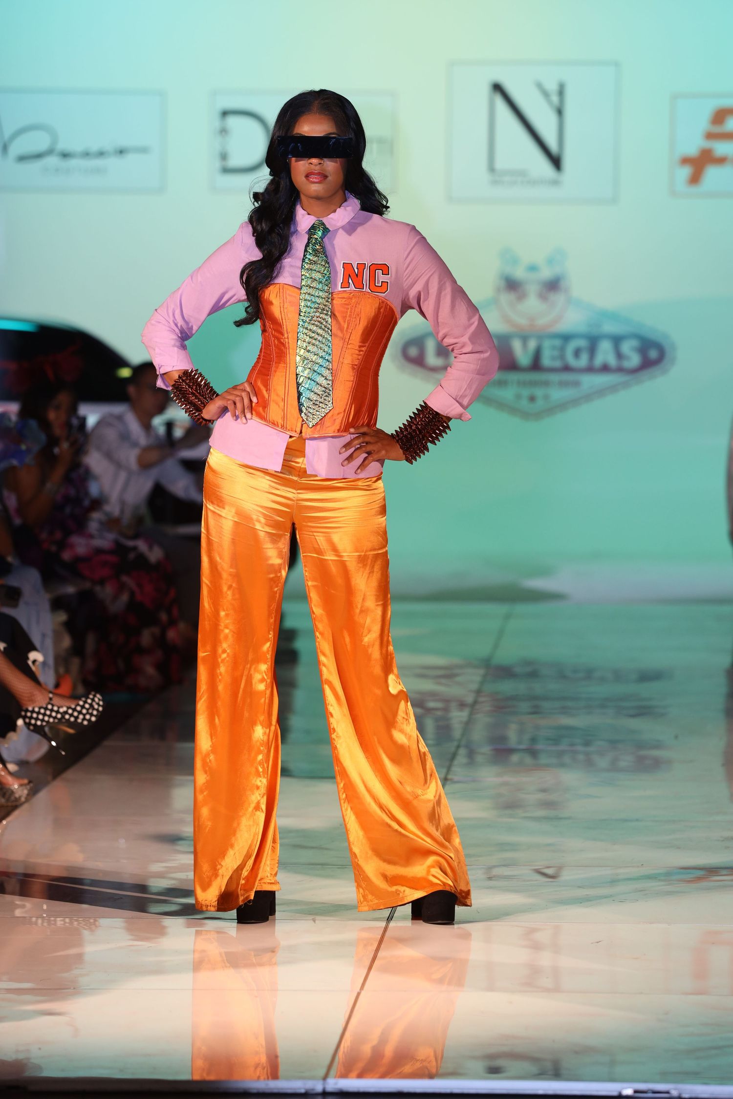 Orange satin pants paired with pink jacket shown on aqua-lit fashion runway.