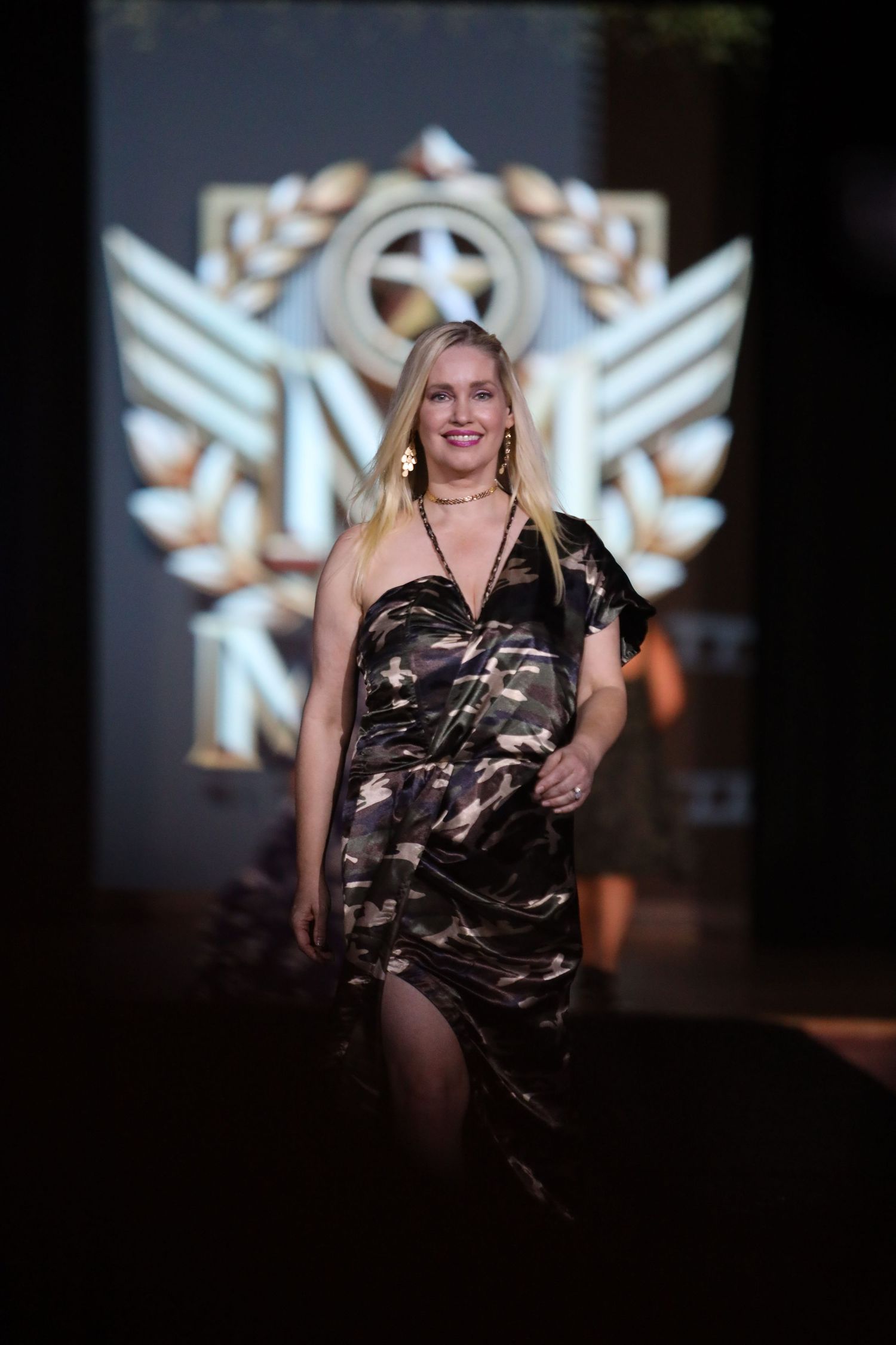 Model walks runway in camouflage evening wear during fashion show.