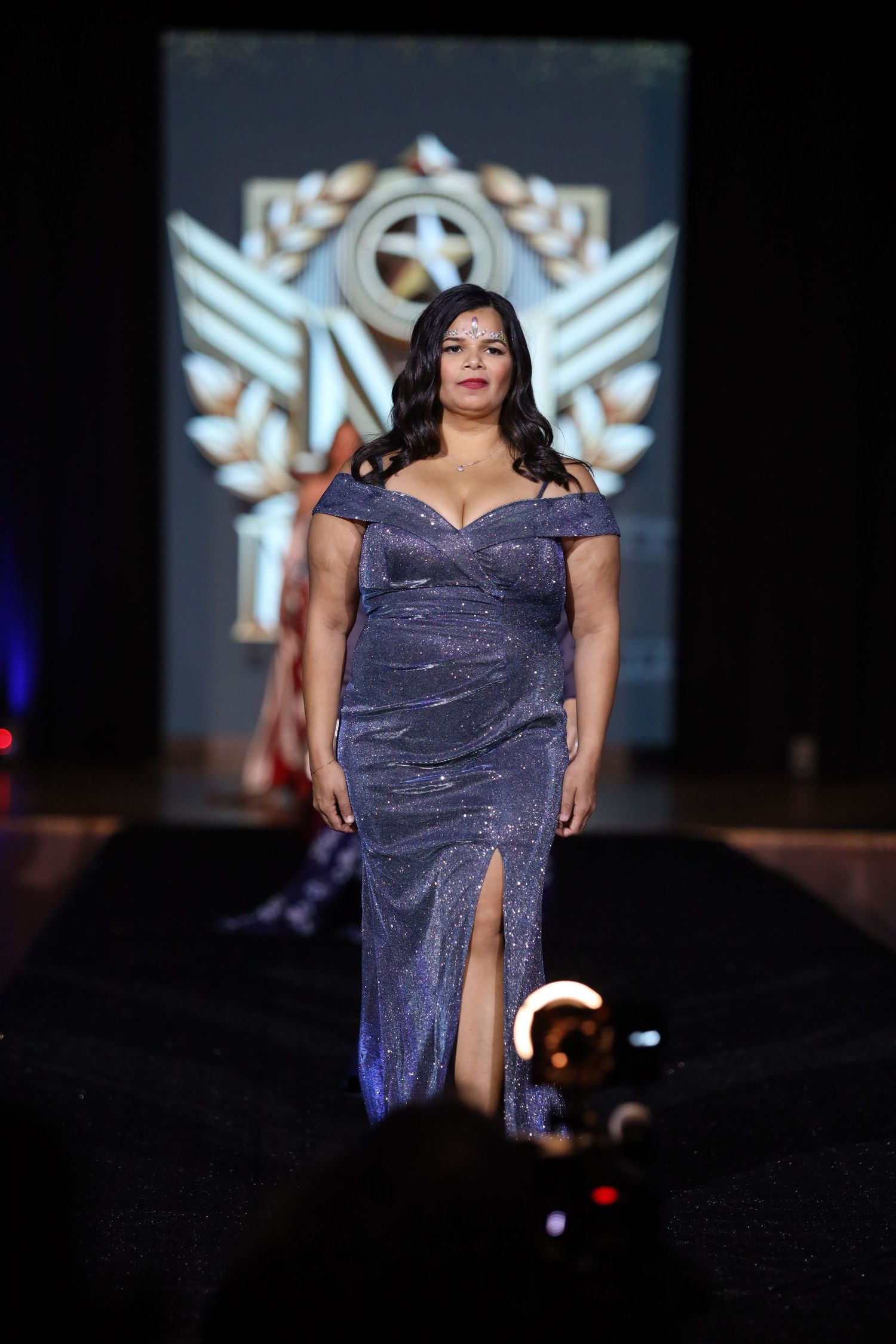 Model showcases sparkling purple evening gown on fashion runway.