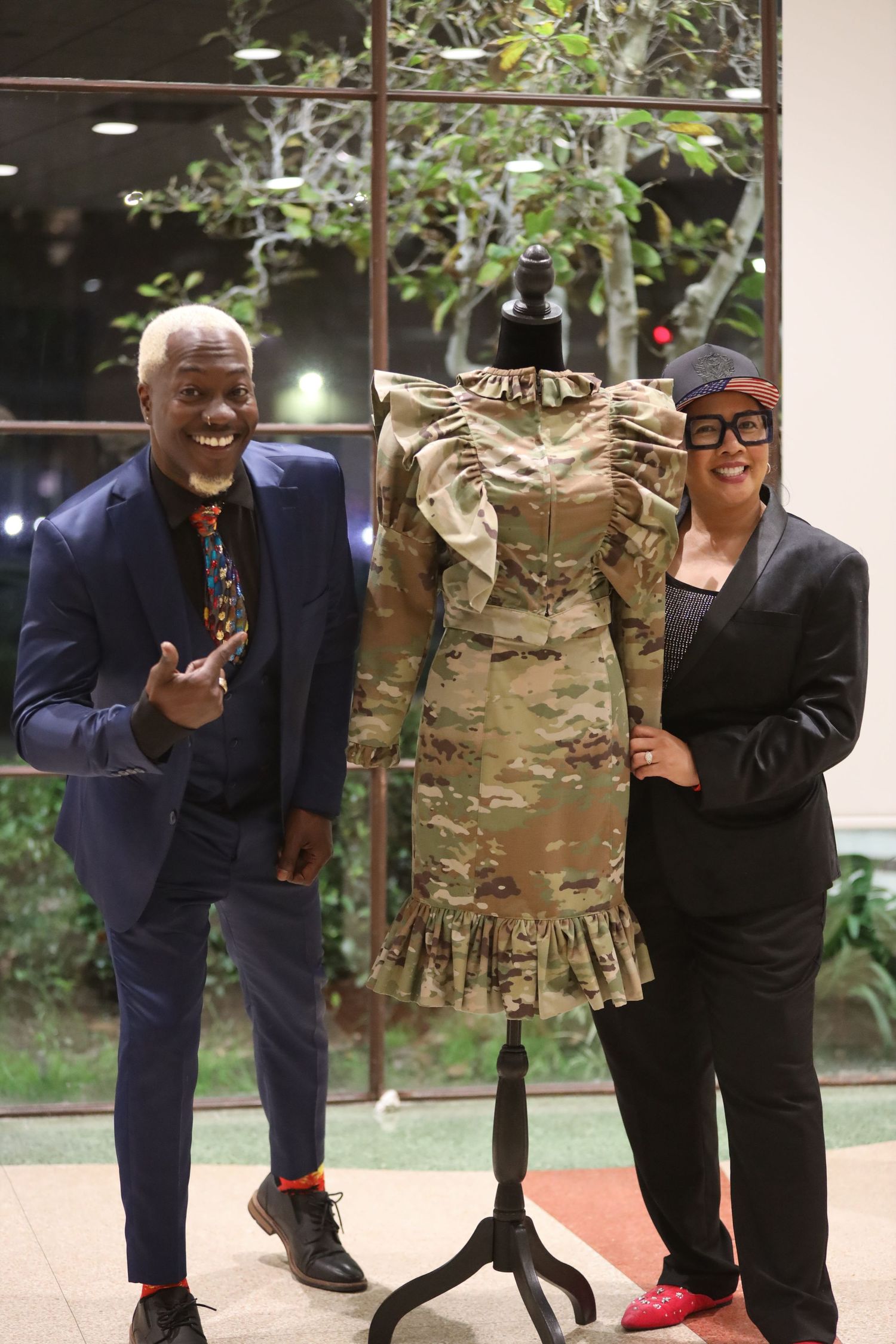 Playful fashion show moment with camouflage dress display and navy blazer.