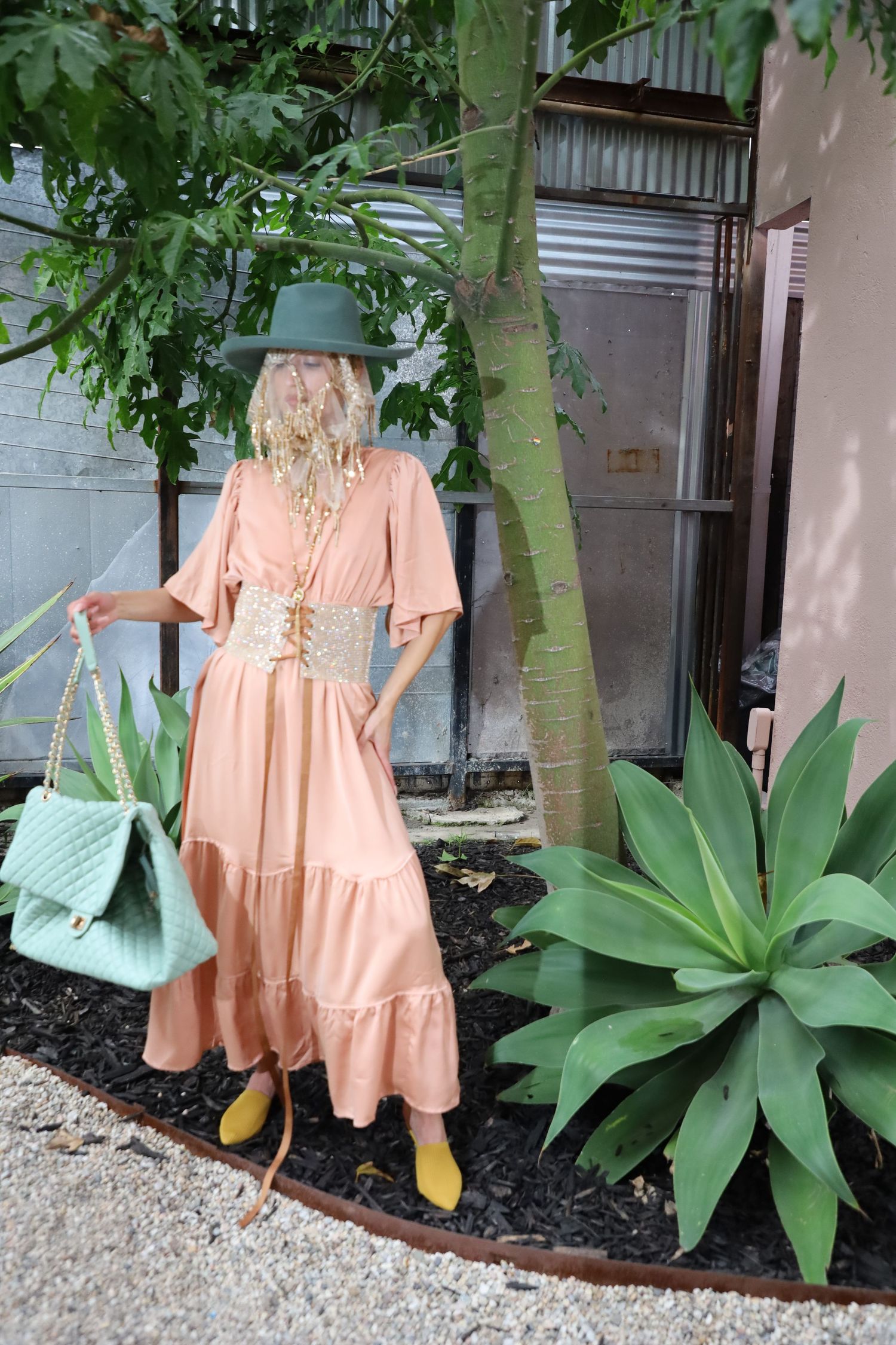 Peach-colored tiered maxi dress styled with yellow shoes and mint accessories against garden backdrop.
